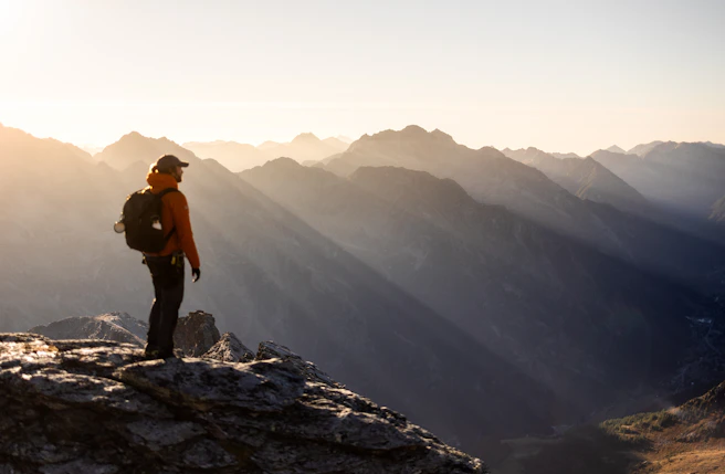 Hiker on mountain peak at sunrise with sun rays.