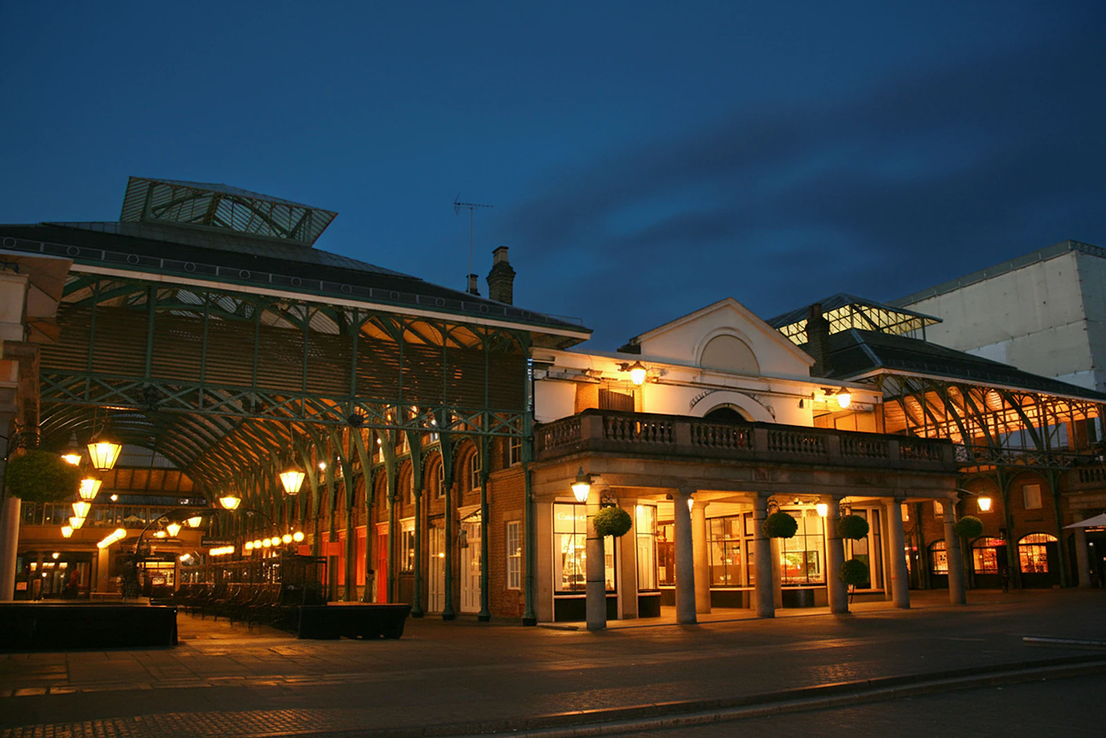 Photograph of Covent Garden’s covered market glowing with warm lights beneath an evening sky.