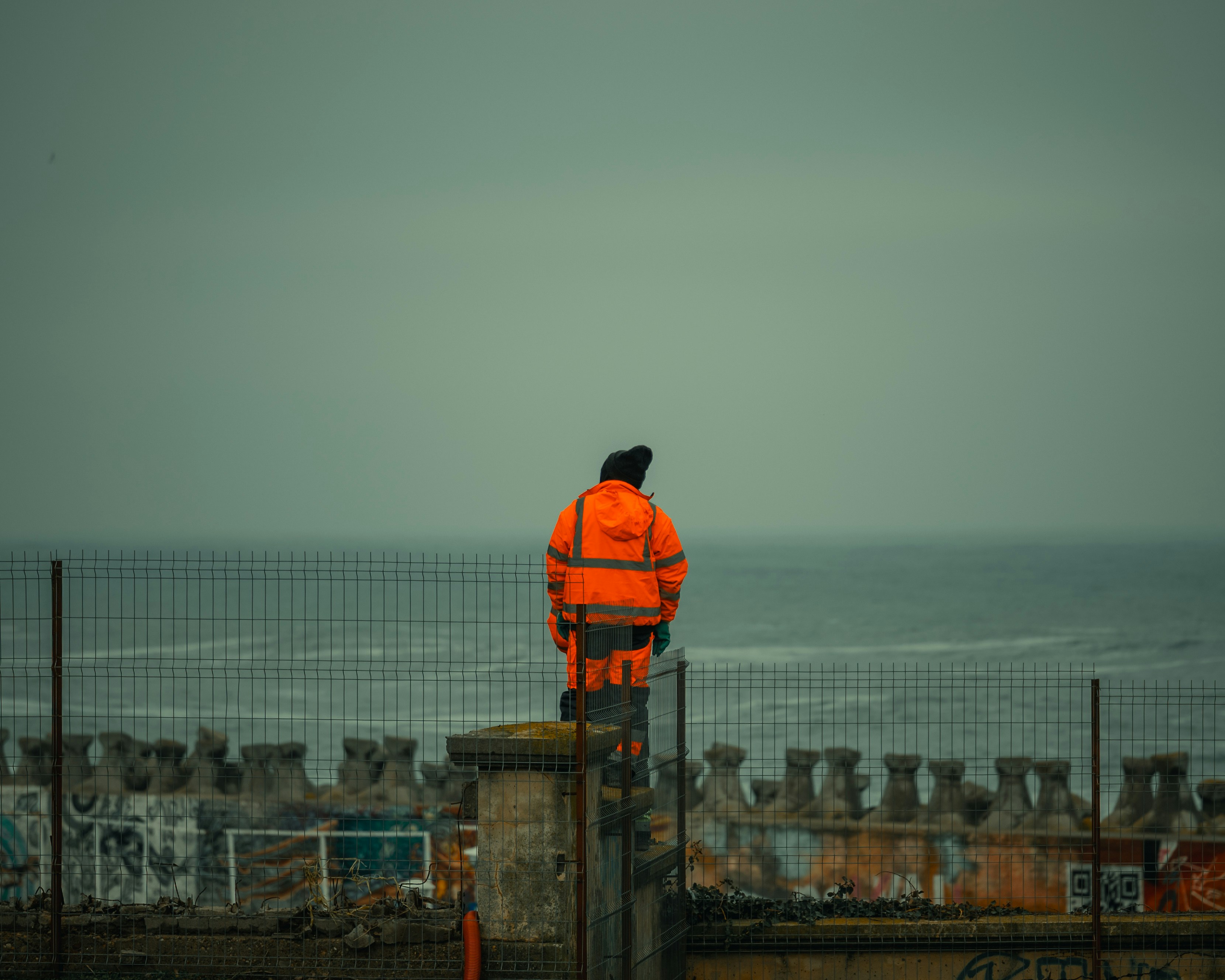 A person in an orange jacket stands on a wall.
