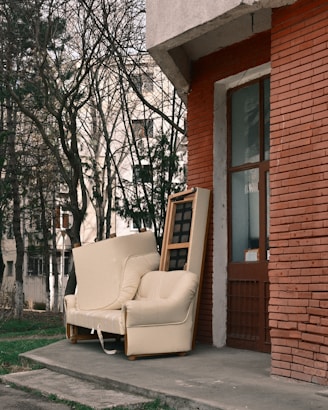 An old armchair and sofa left outside a brick building.