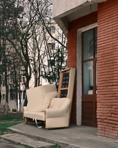 An old armchair and sofa left outside a brick building.