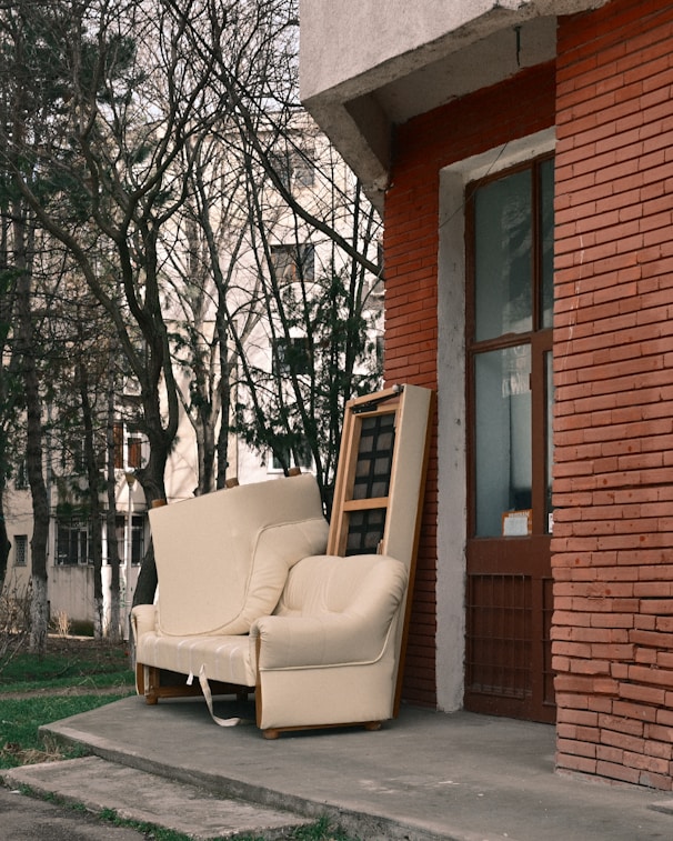An old armchair and sofa left outside a brick building.