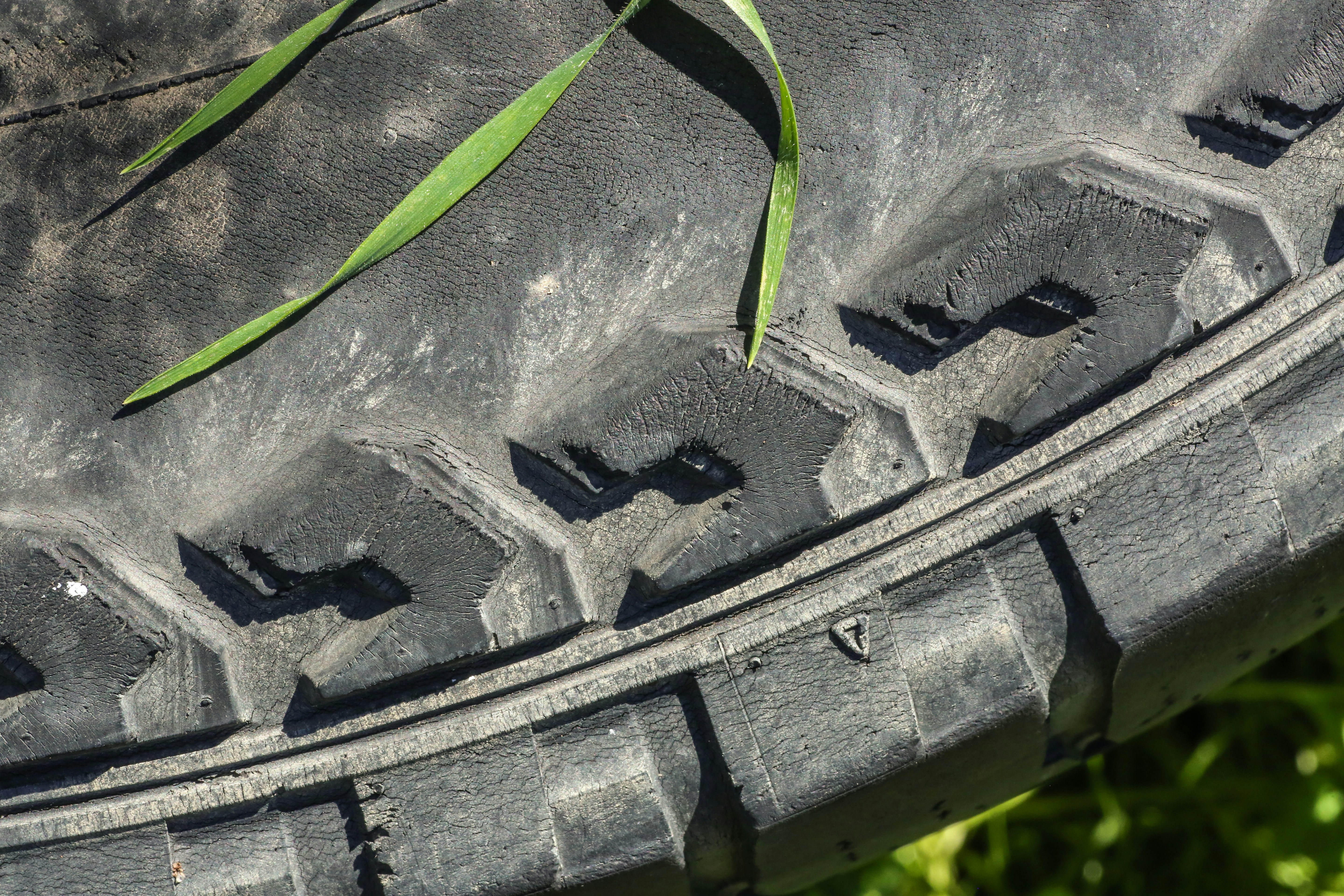 Close-up of a worn tire tread with grass blades.