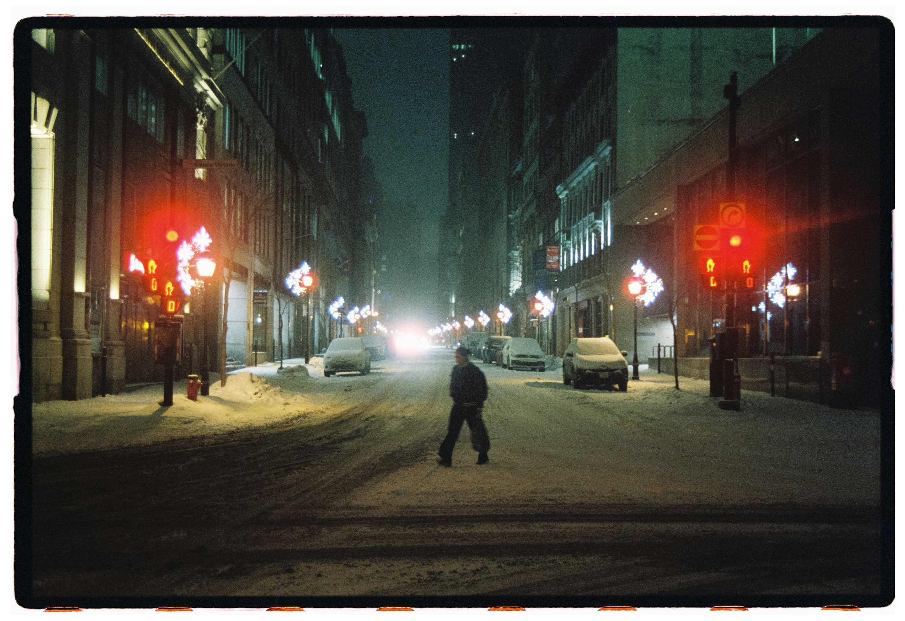 A person walks across a snowy city street at night.