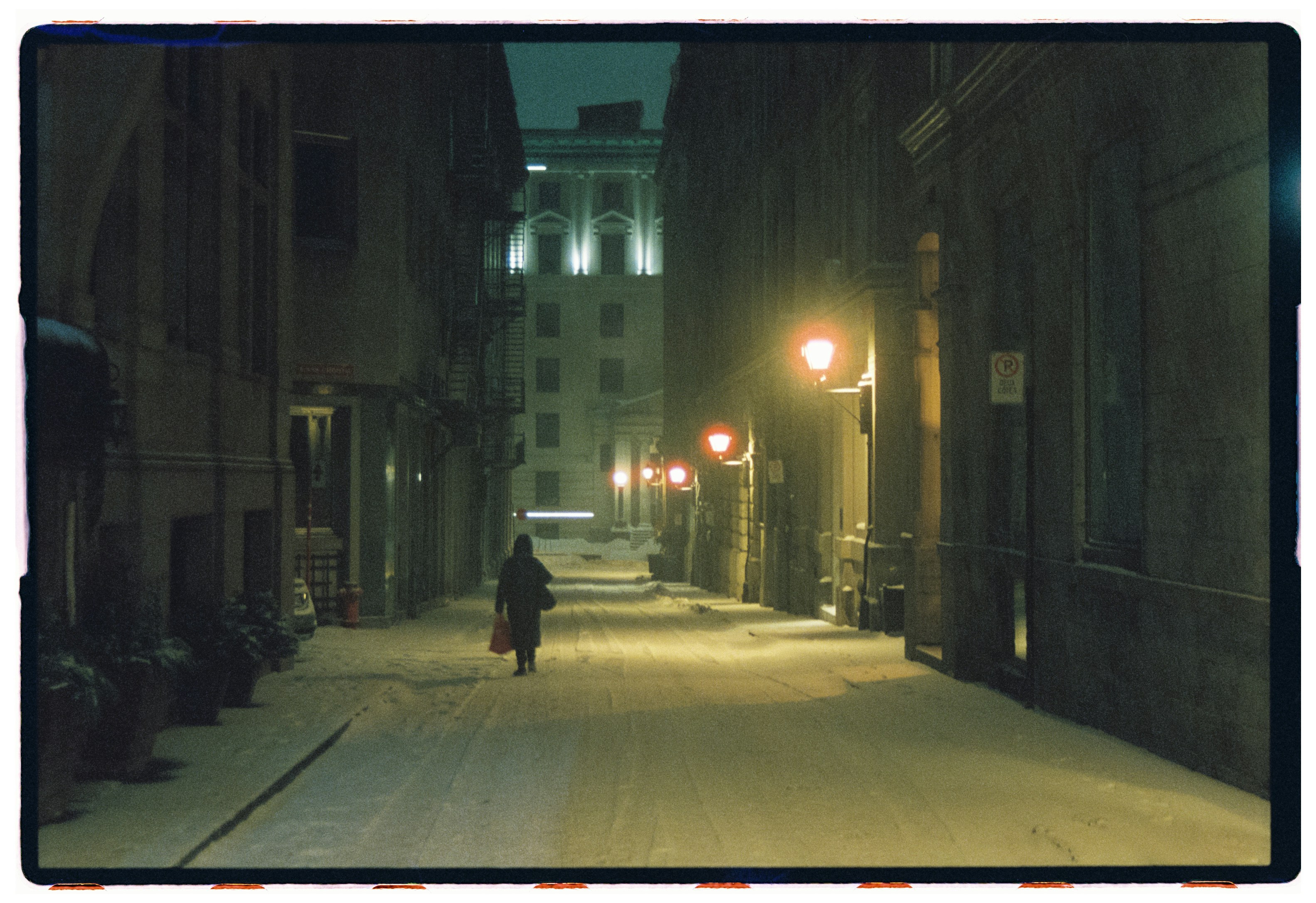 A person walks down a snowy street at night.