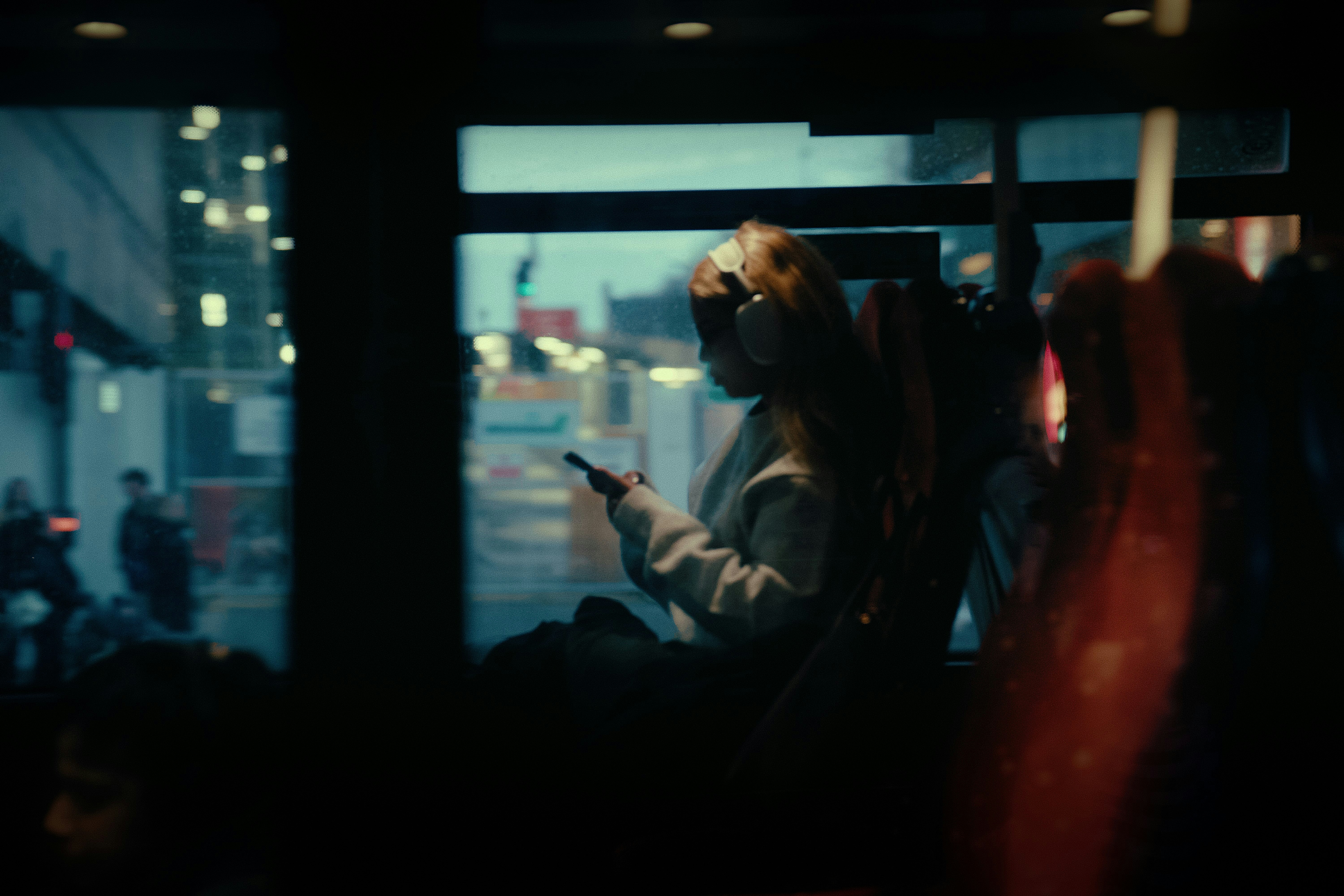 A woman sitting on a bus, looking down at her phone — the exact posture for playing translation guessing games on a long ride