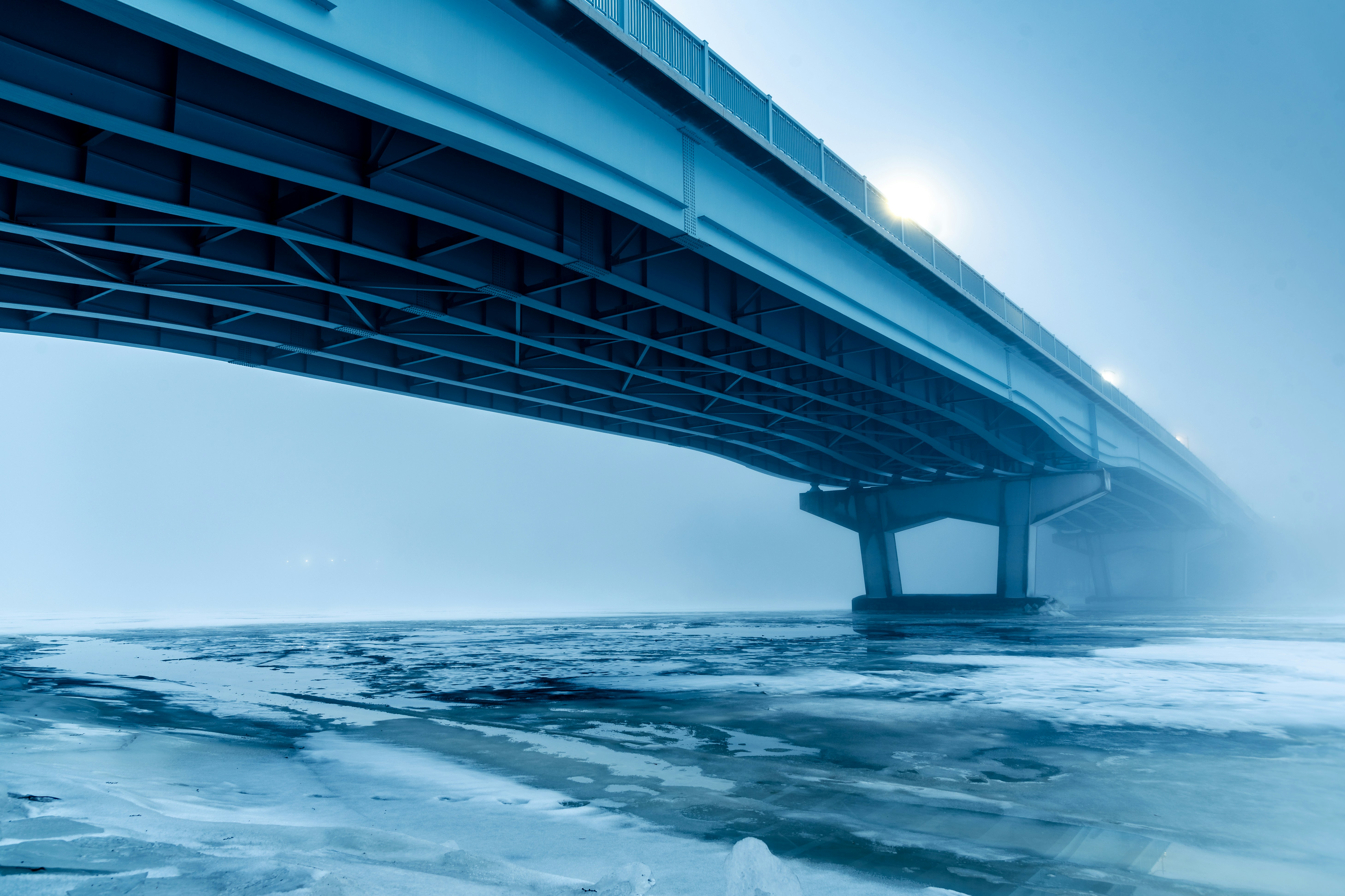 Jembatan besar di atas badan air yang membeku dan berkabut.
