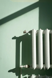 White radiator against a pale green wall with shadows.