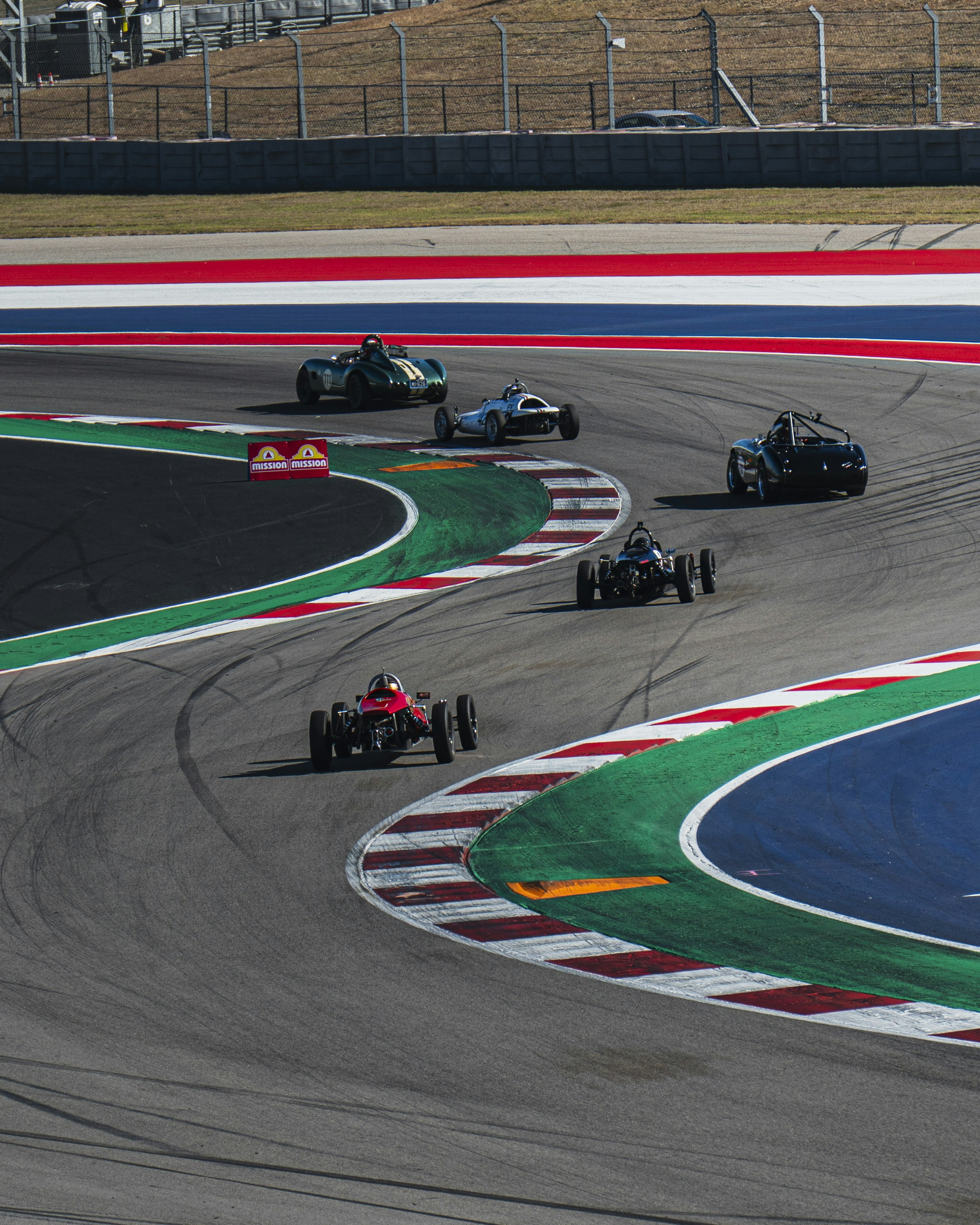 Vintage race cars speed around a colorful track.
