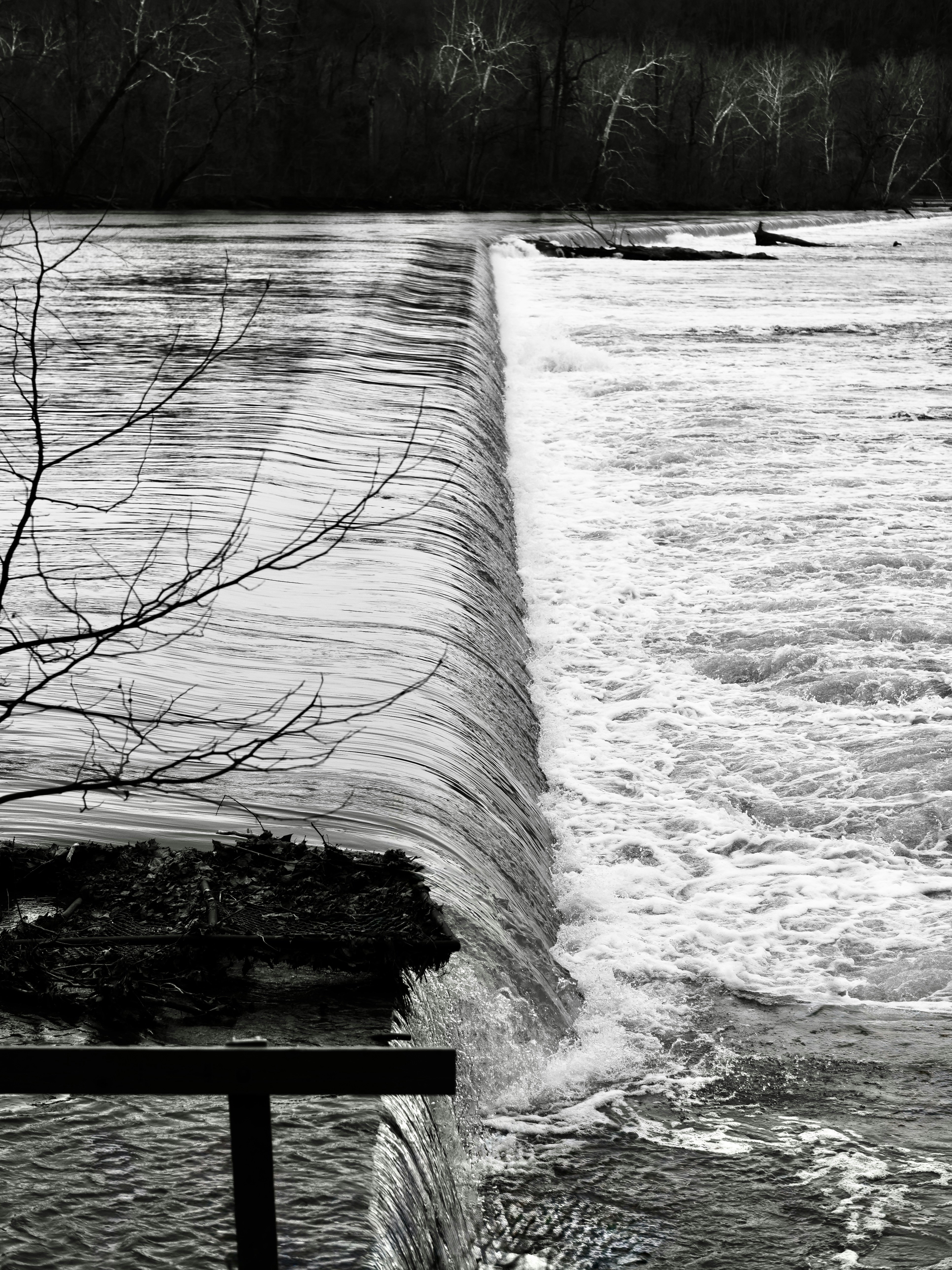 Der Wasserfall fällt schwarz-weiß über einen Betondamm.