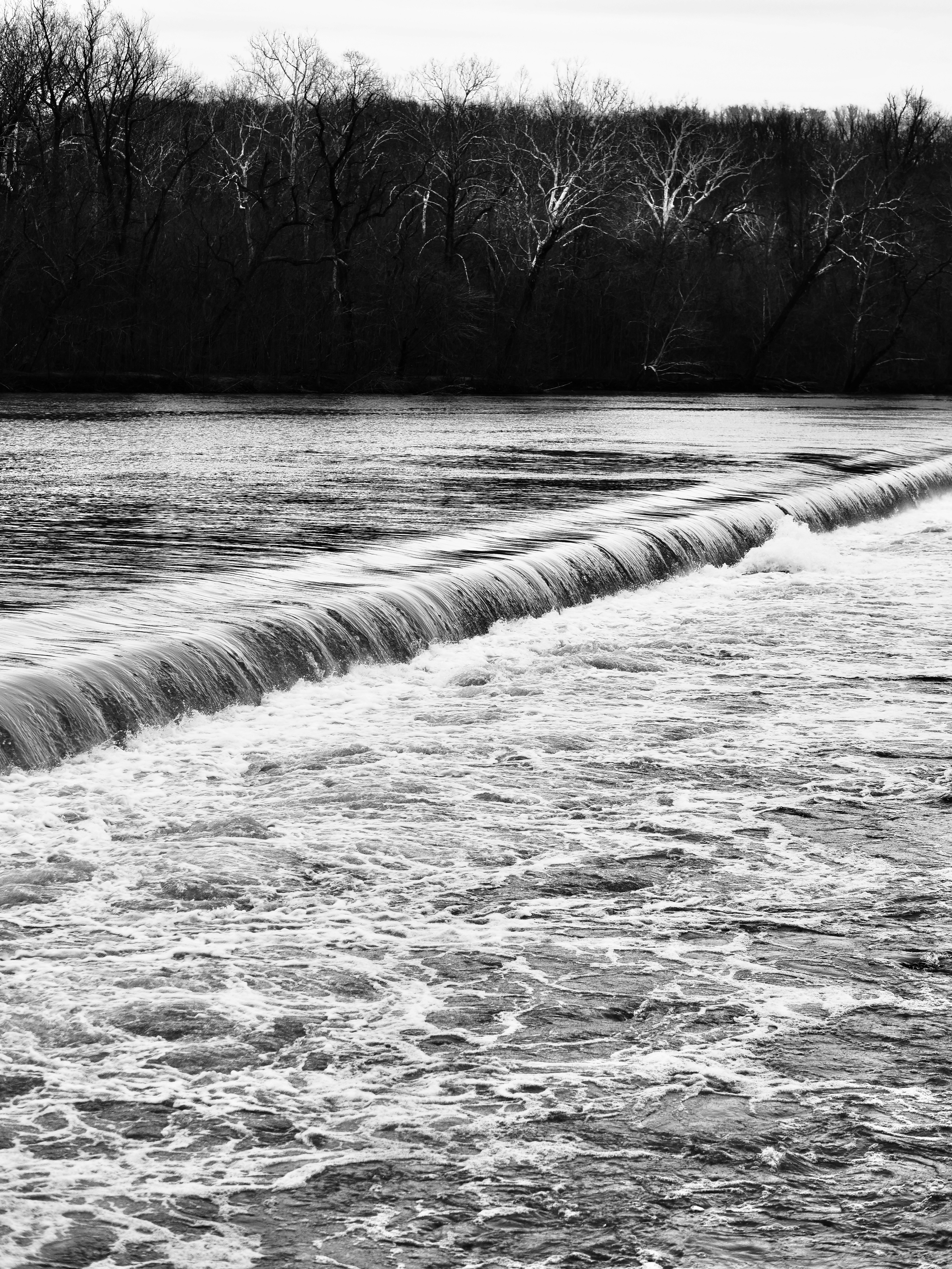 Wasserfall über einen Damm mit Bäumen im Hintergrund