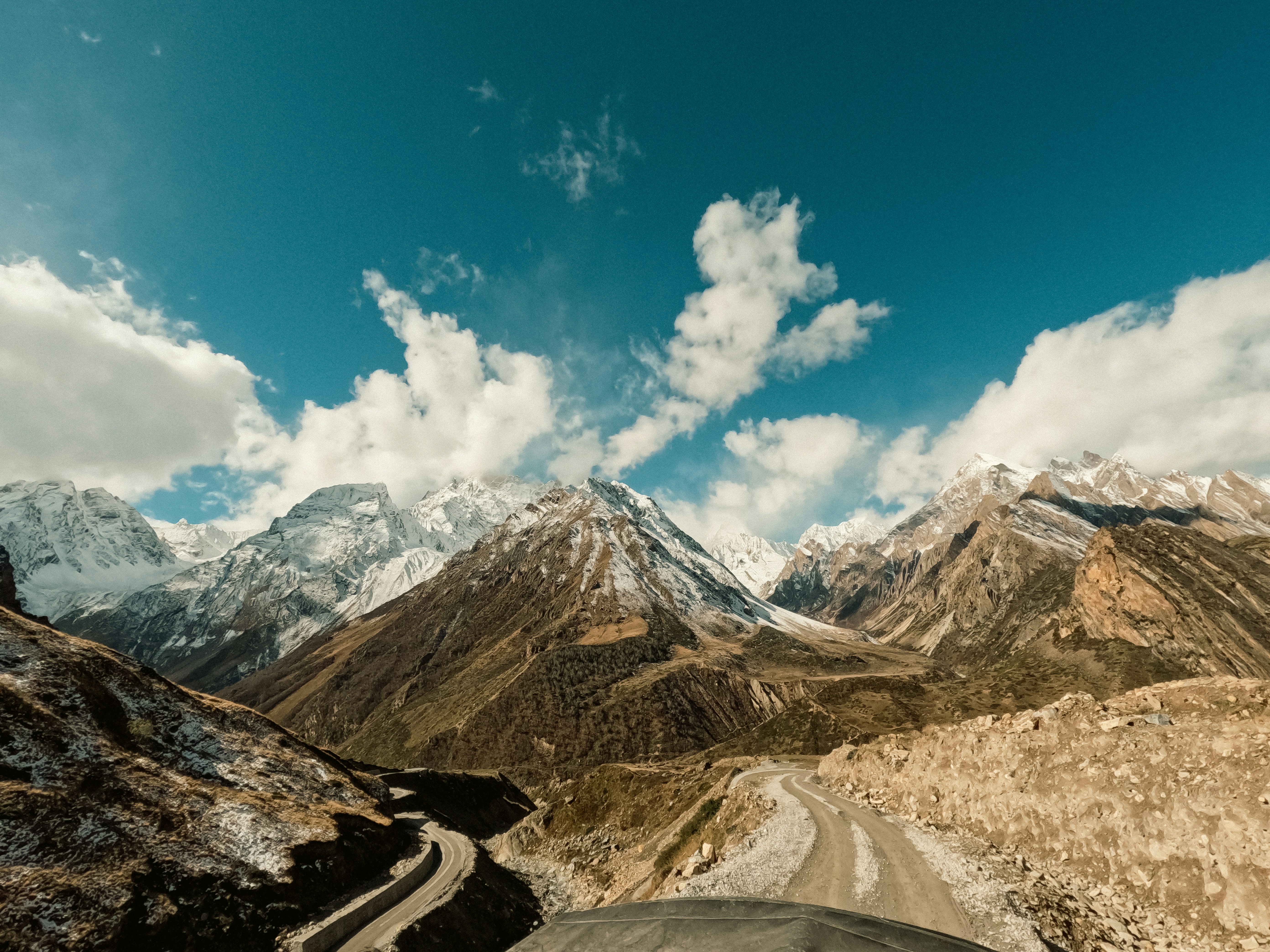 A wide shot of the Himalayan mountains, emphasizing their grandeur and fragility, with a small section of a newly built road cutting through.