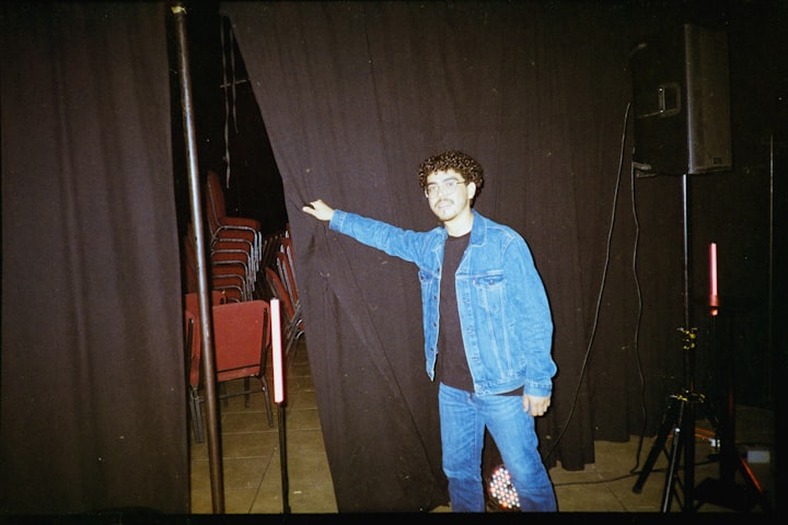 A figure waiting in the wings behind a dark curtain, off-stage moment, anonymized