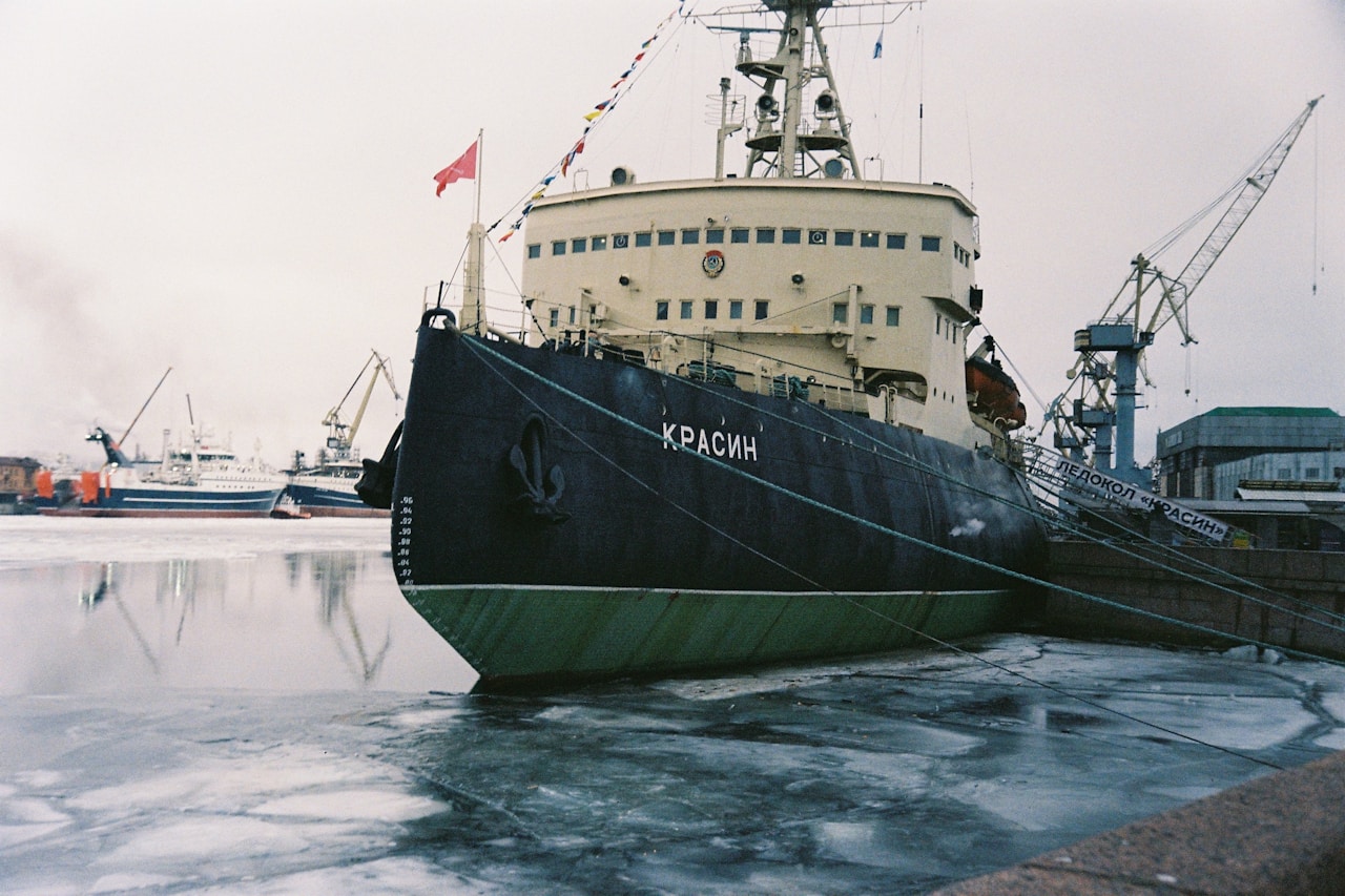An icebreaker moored in a frozen harbour, with ice-covered water and port cranes behind