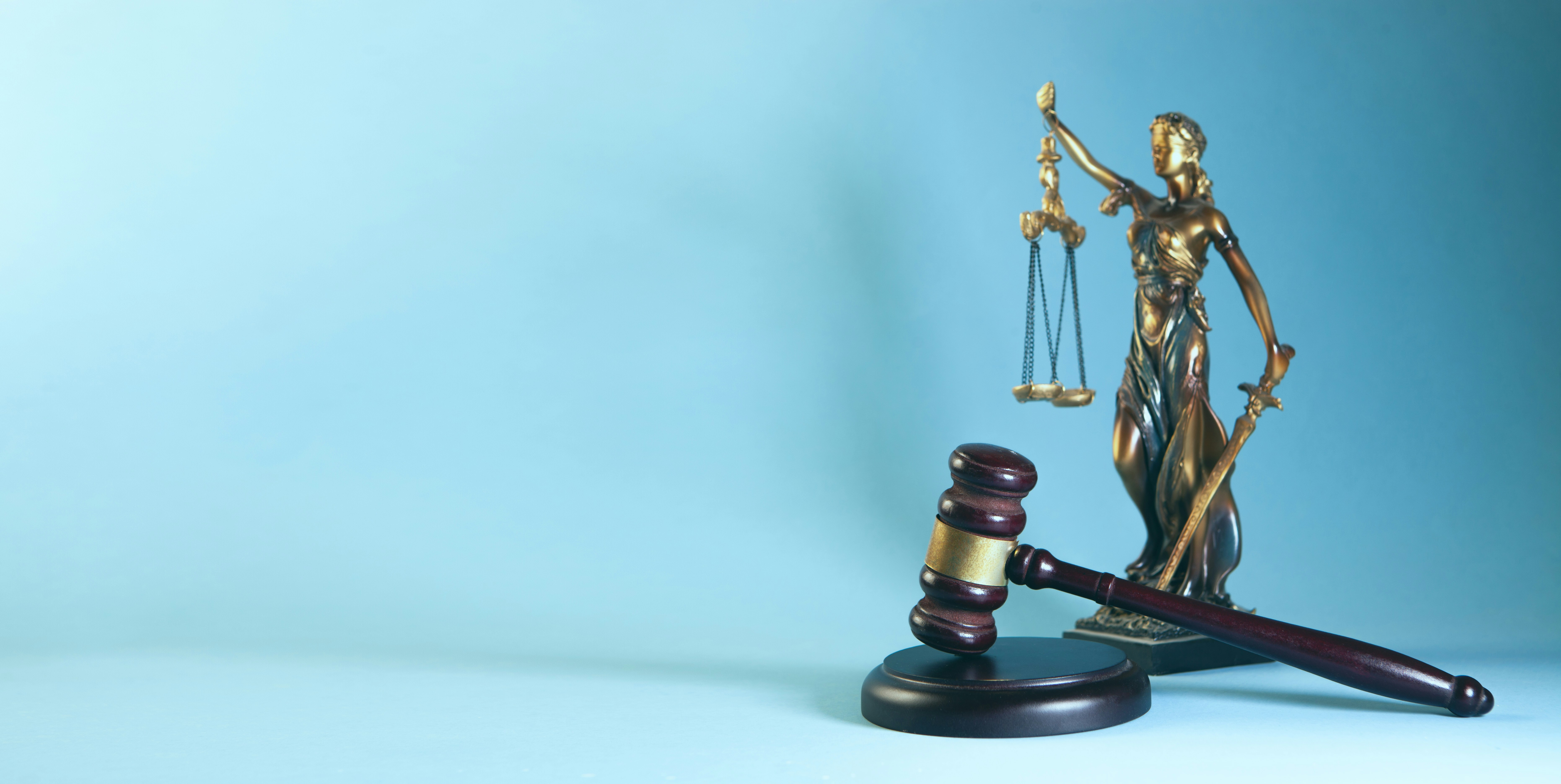 Brass scales of justice and a wooden gavel on a blue background symbolizing law and legal authority