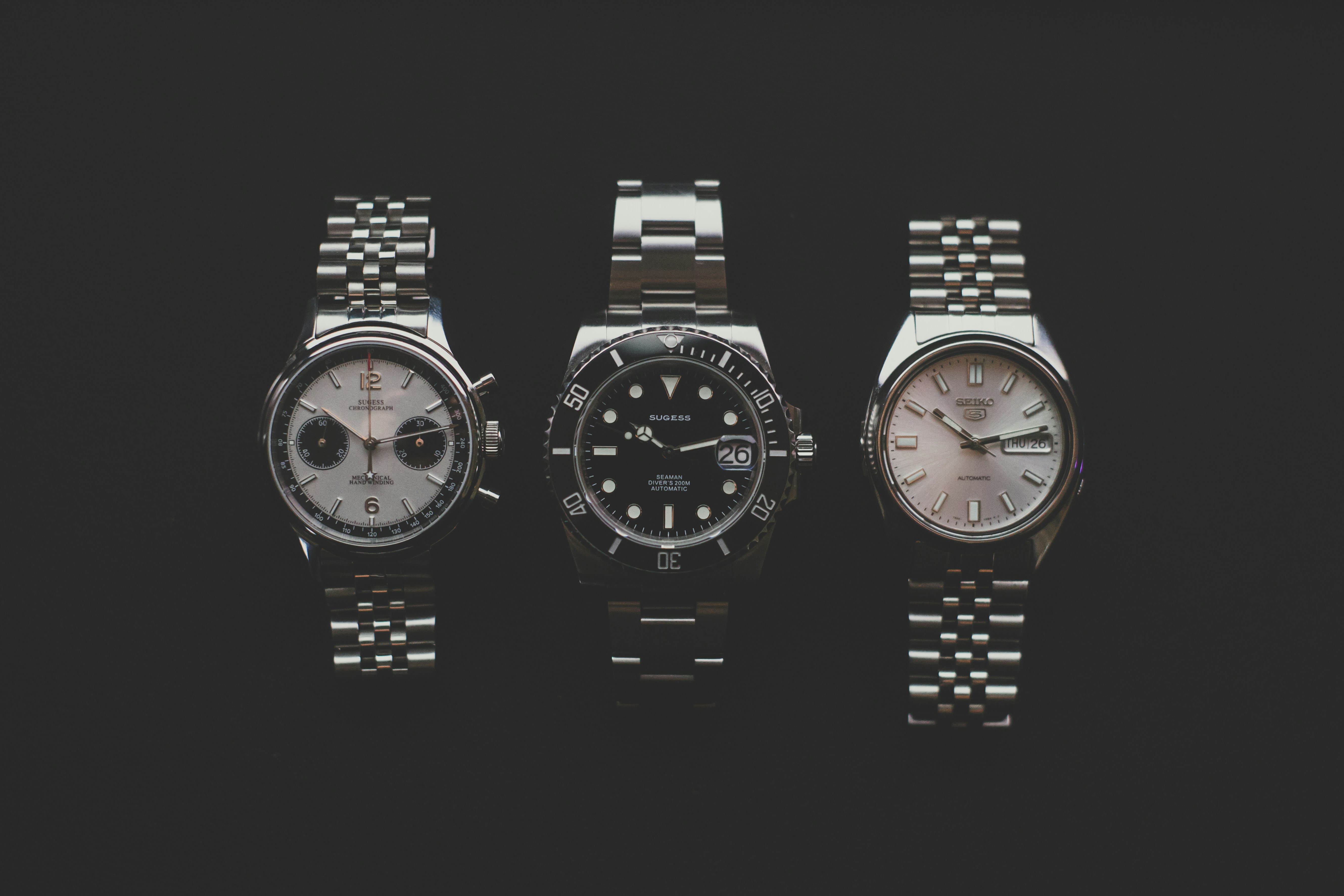 Three metal wristwatches on a dark surface
