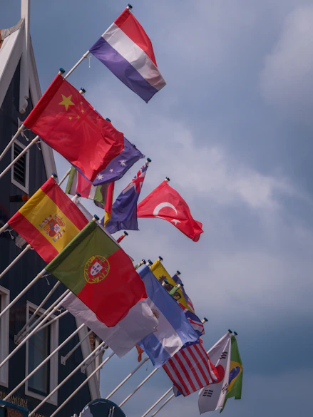 Various national flags flying against a cloudy sky
