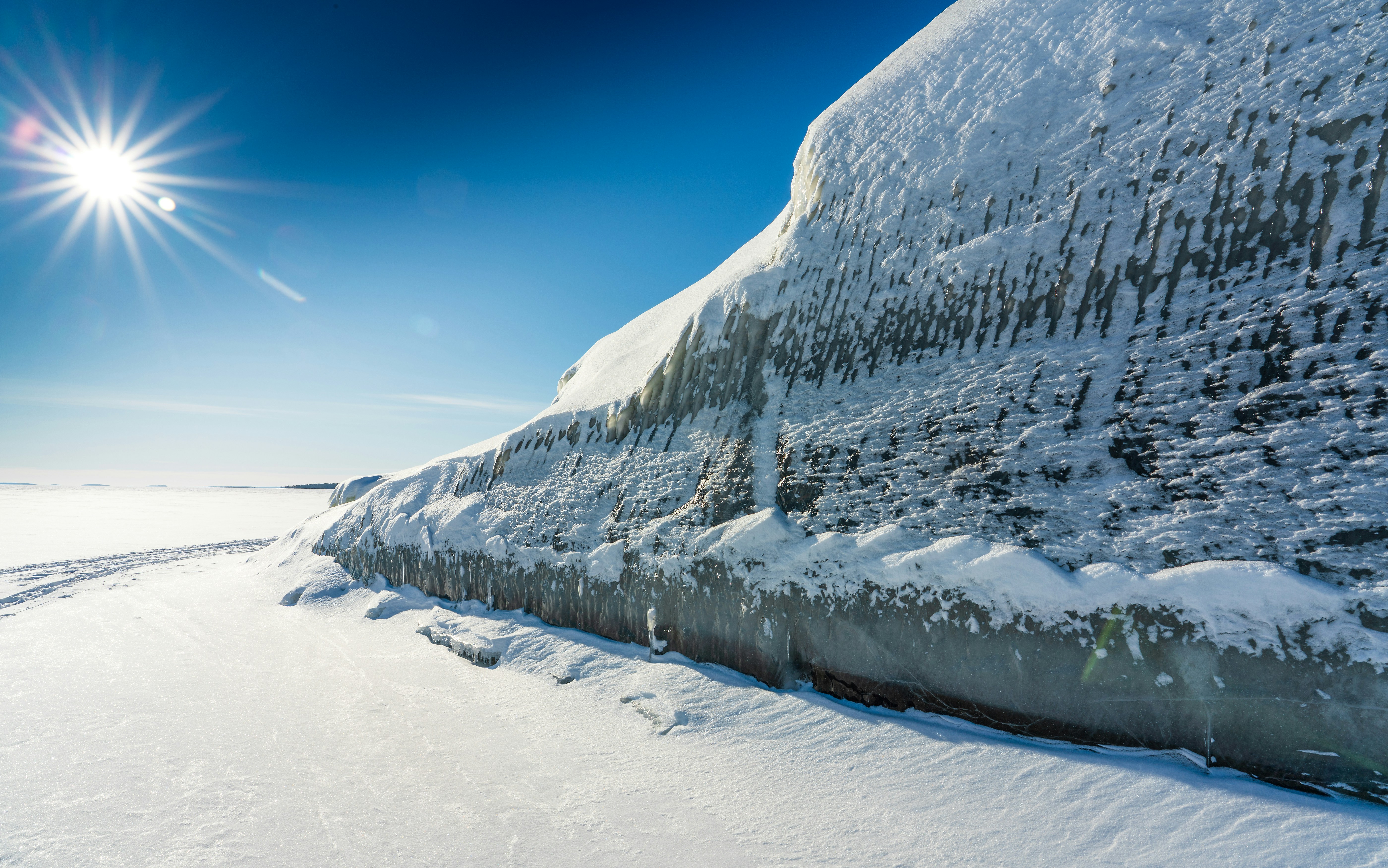 Sun shines on icy cliff by frozen lake in winter