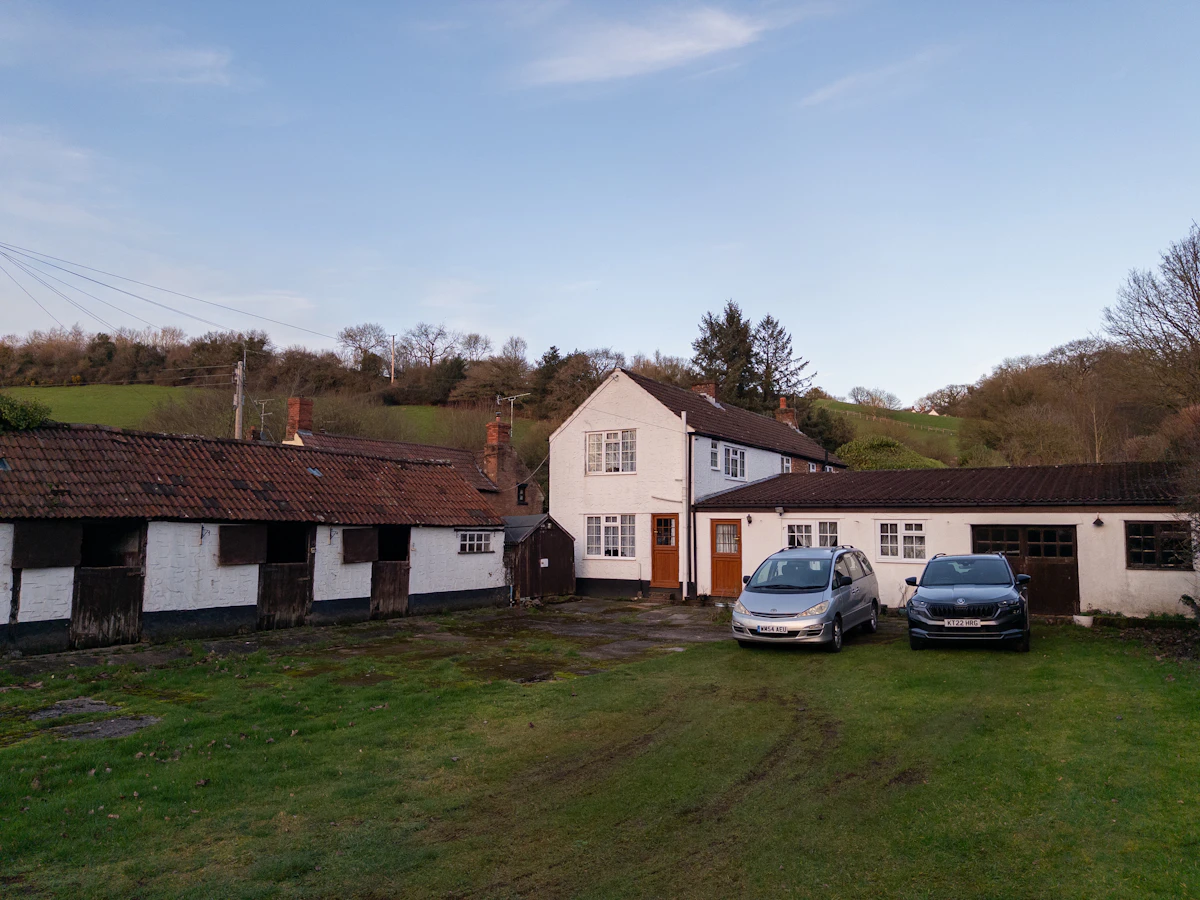 Rural farmhouse with stables and cars parked outside
