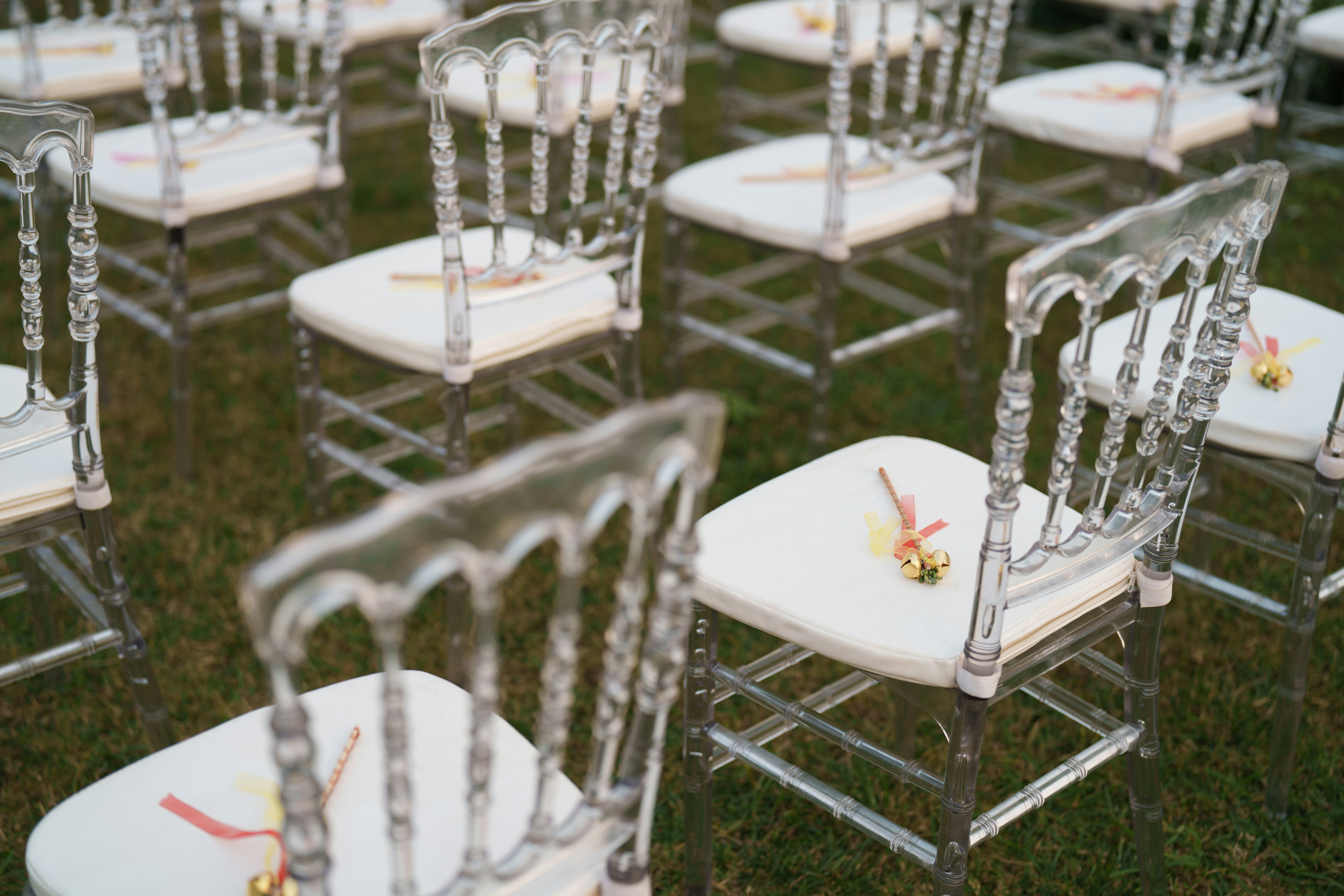 Reihen leerer, durchsichtiger Stühle mit weißen Kissen auf dem Gras.