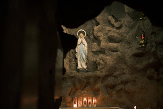Statue of mary in a grotto with lit candles.