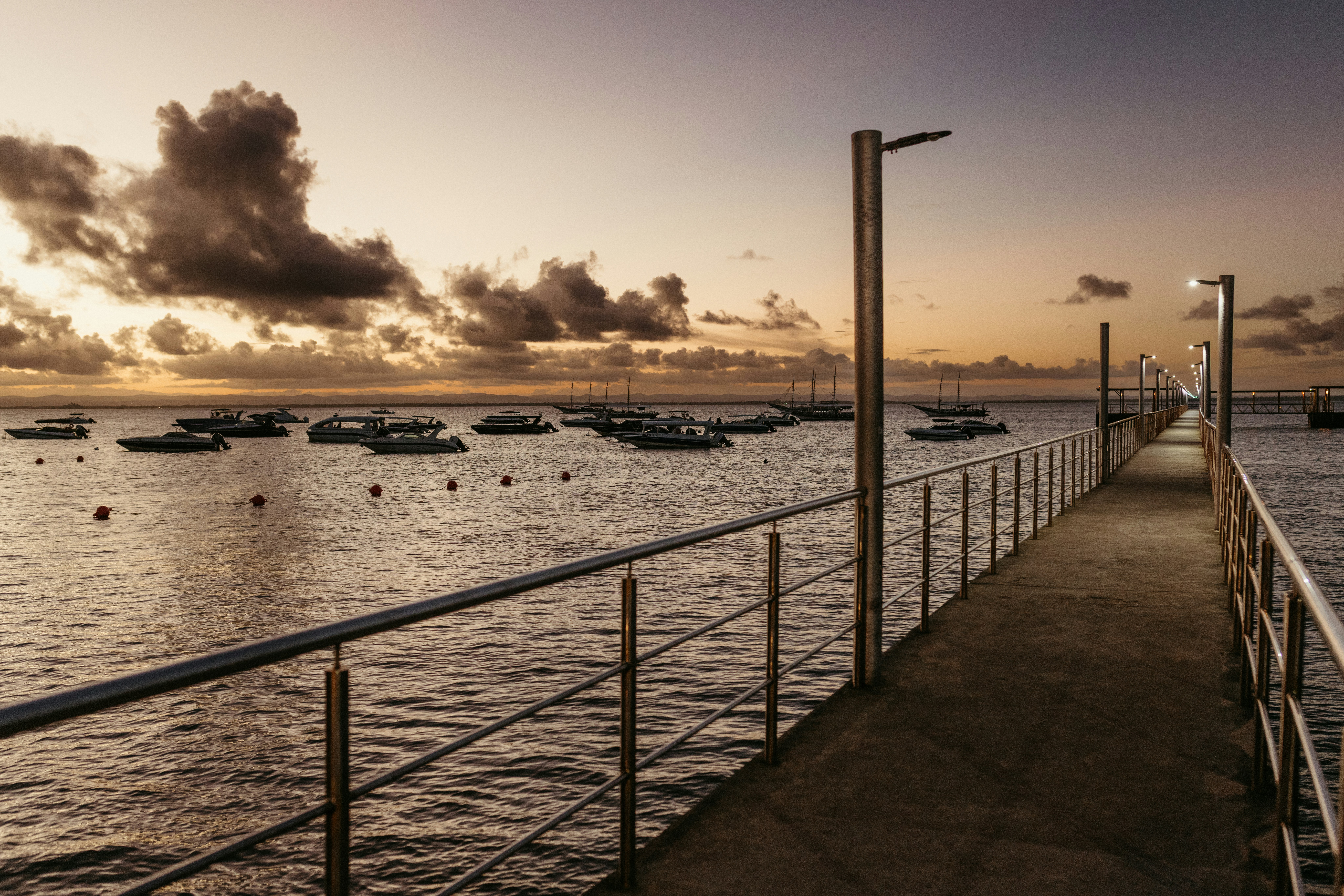 Pier extending over the ocean with boats at sunset