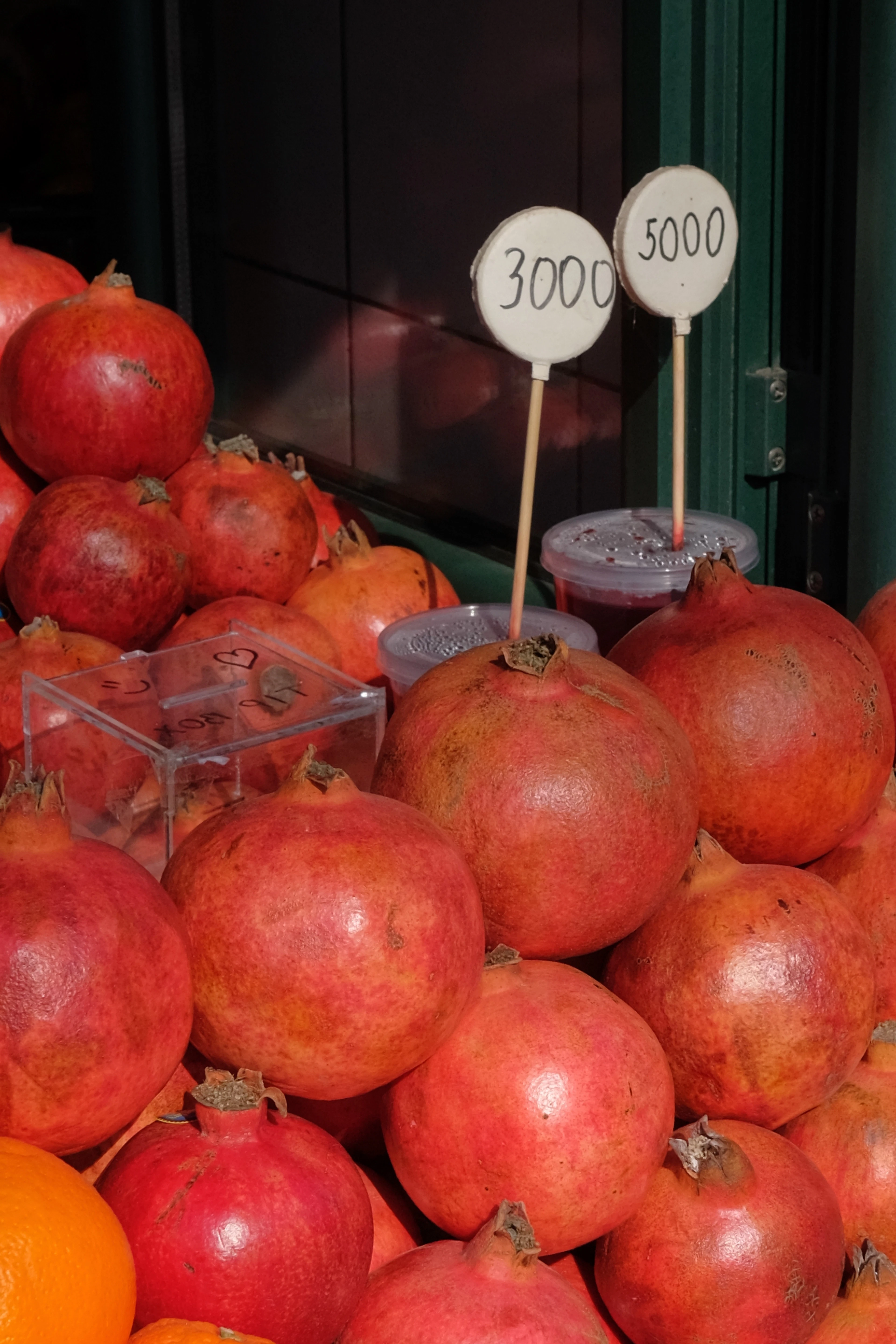 Ripe pomegranates piled high on a market stall in Yerevan, with handwritten cards showing prices in Armenian dram.