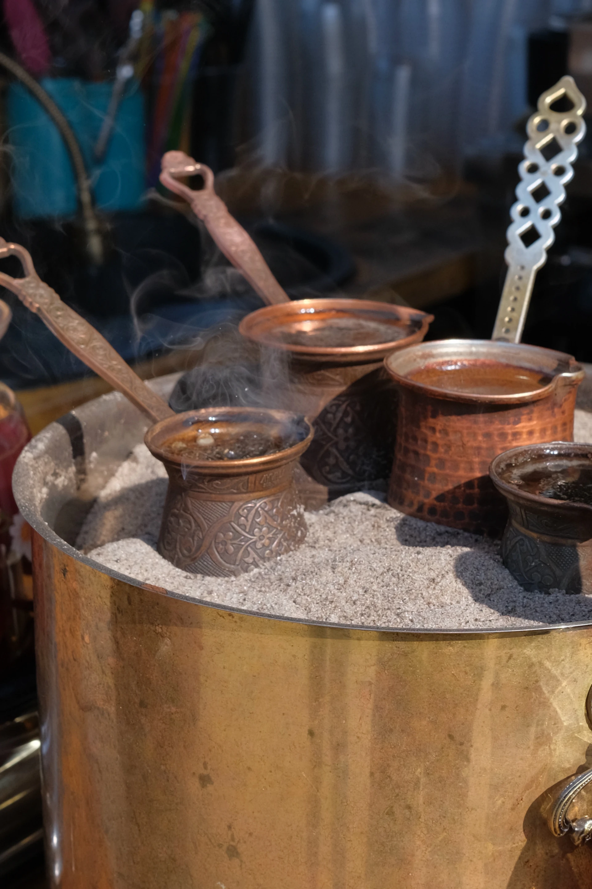 A hand-hammered copper Jazve resting on hot sand with rising steam