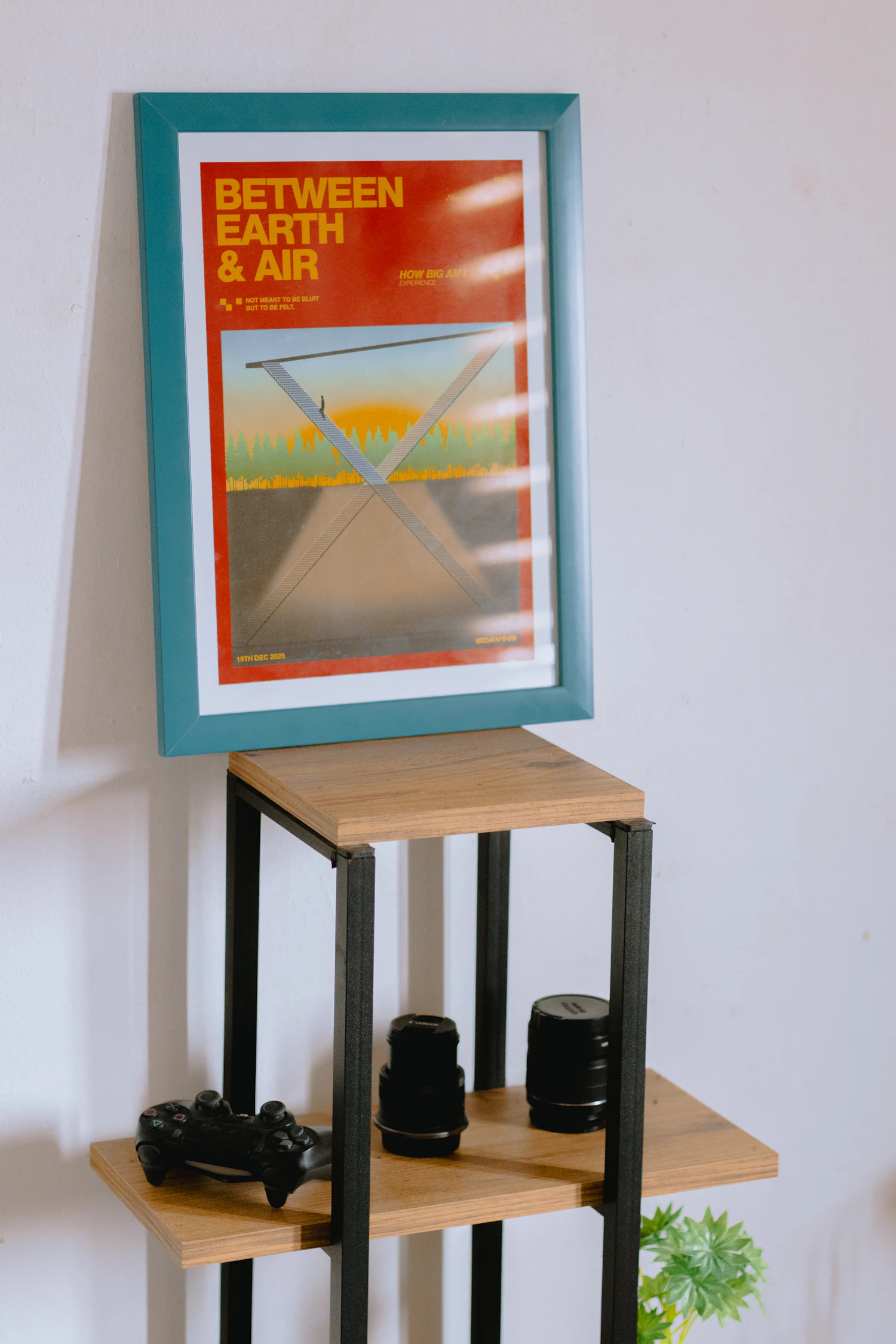 A framed print propped on a shelf beside camera lenses