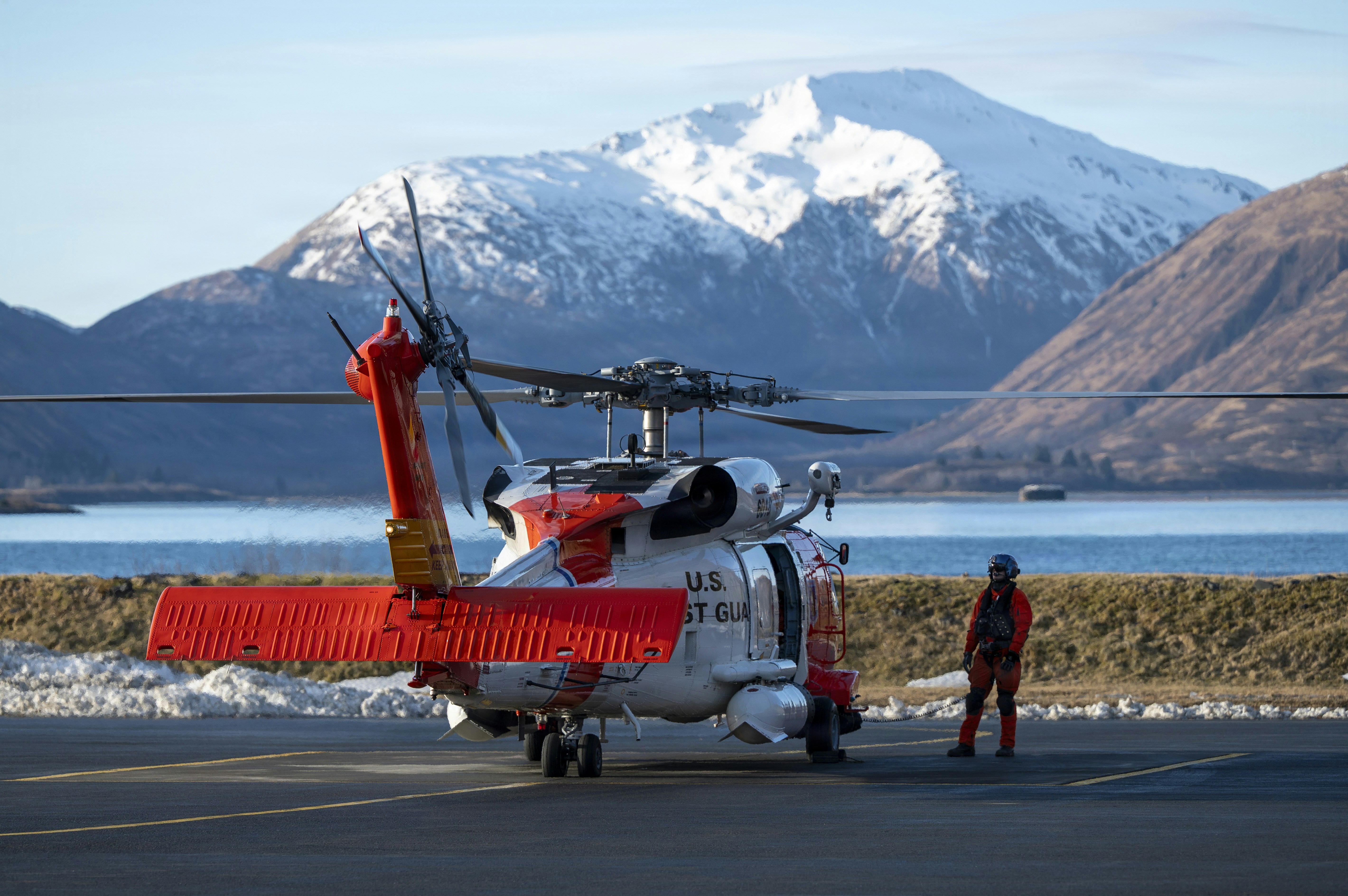 Coast guard helicopter and crew member on tarmac with mountains.