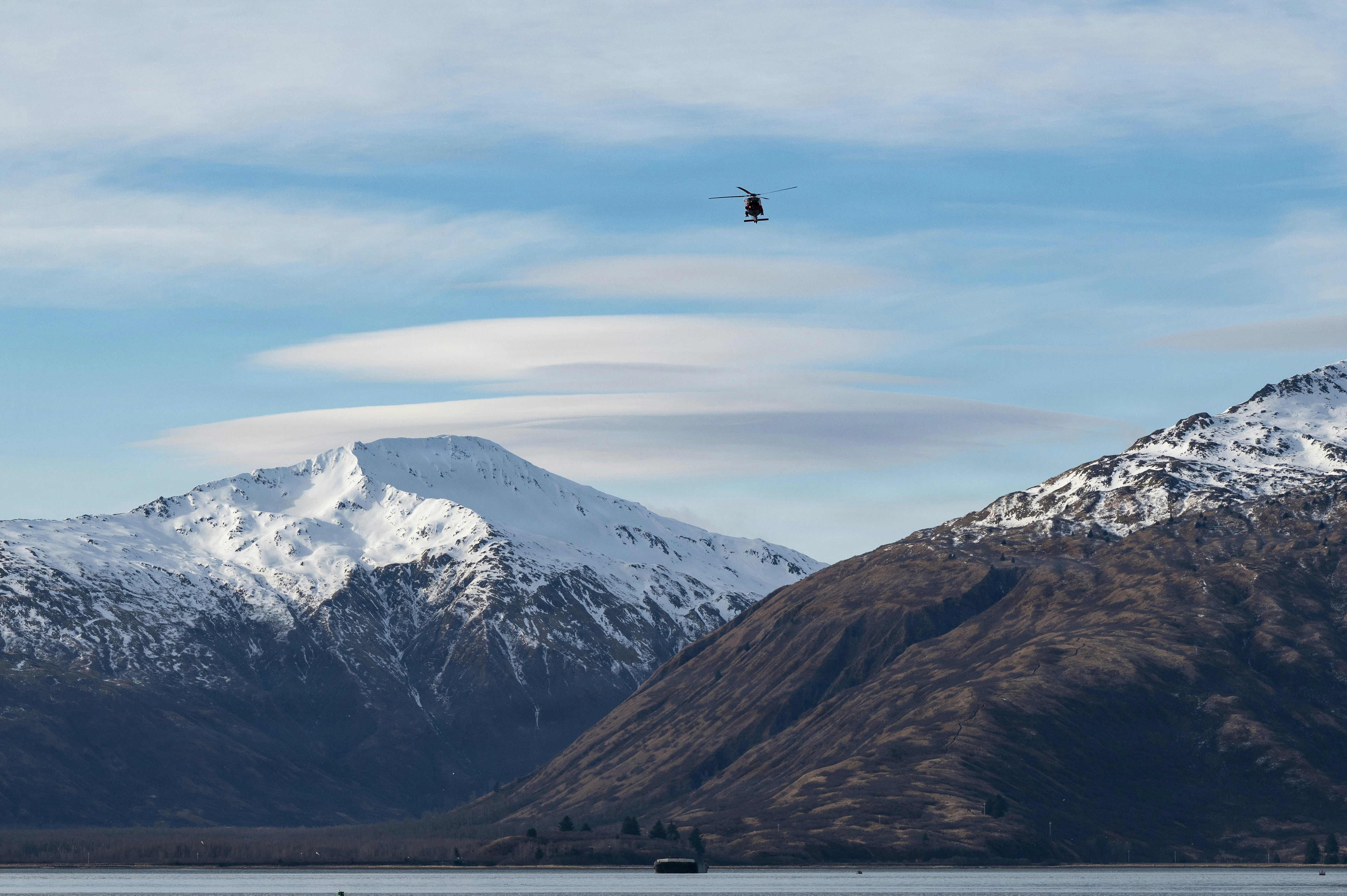A small helicopter flies over snow-capped mountains.