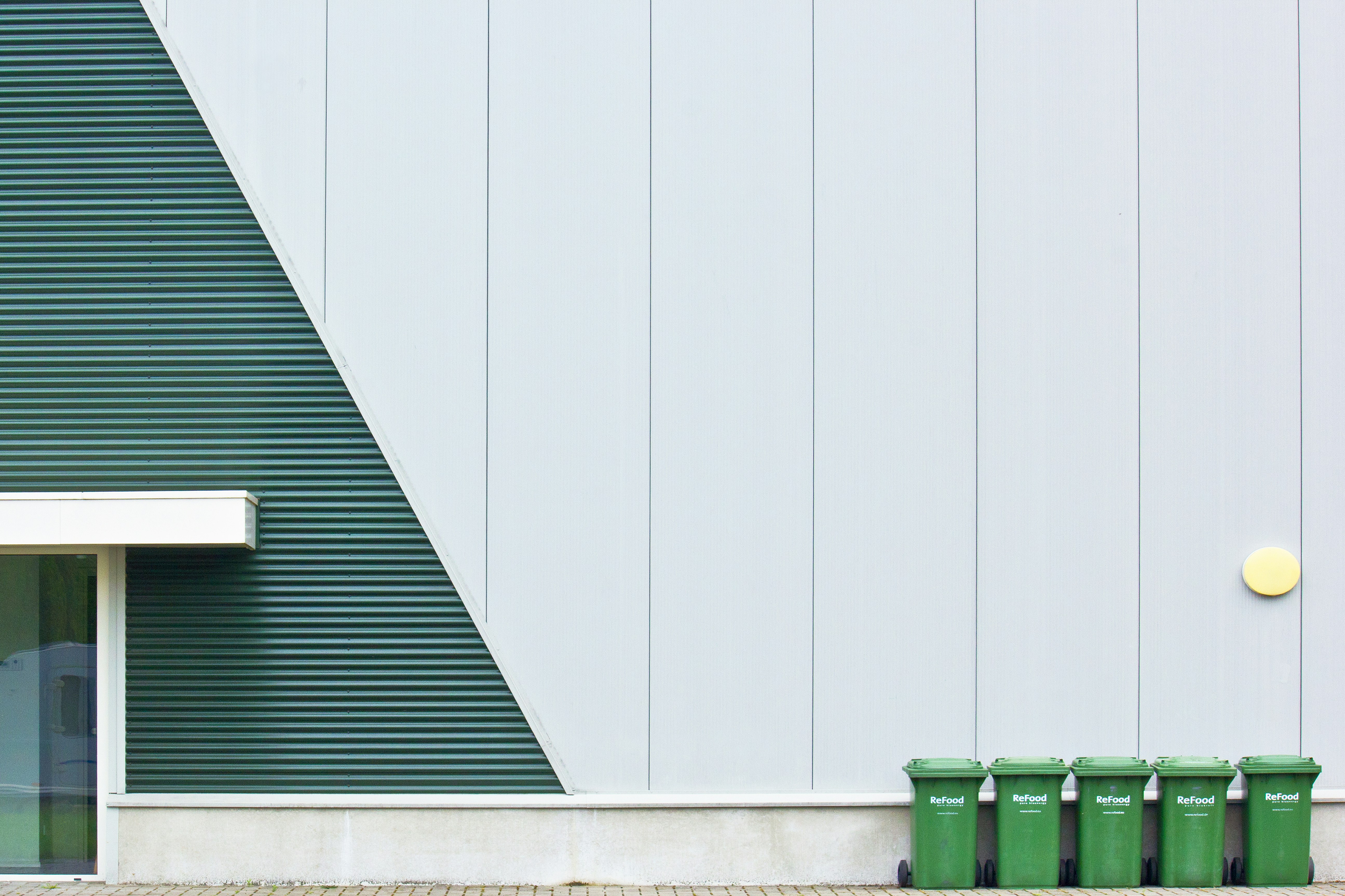 Five green trash cans lined up outside a building