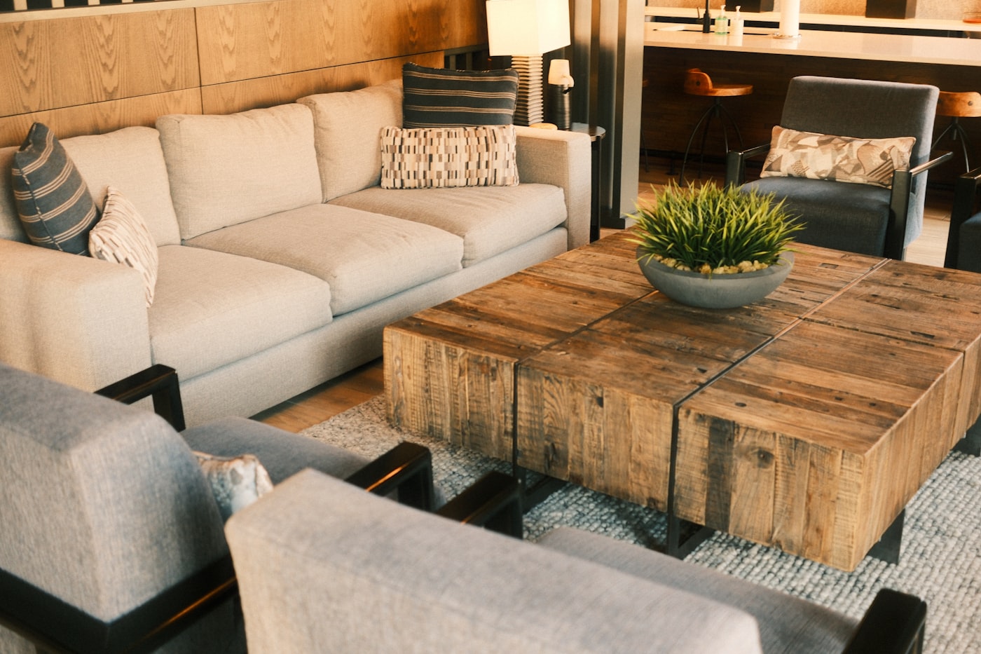 Warm minimalist living room with cream textured sofa, reclaimed wood block coffee table, woven rug, and oak wall paneling