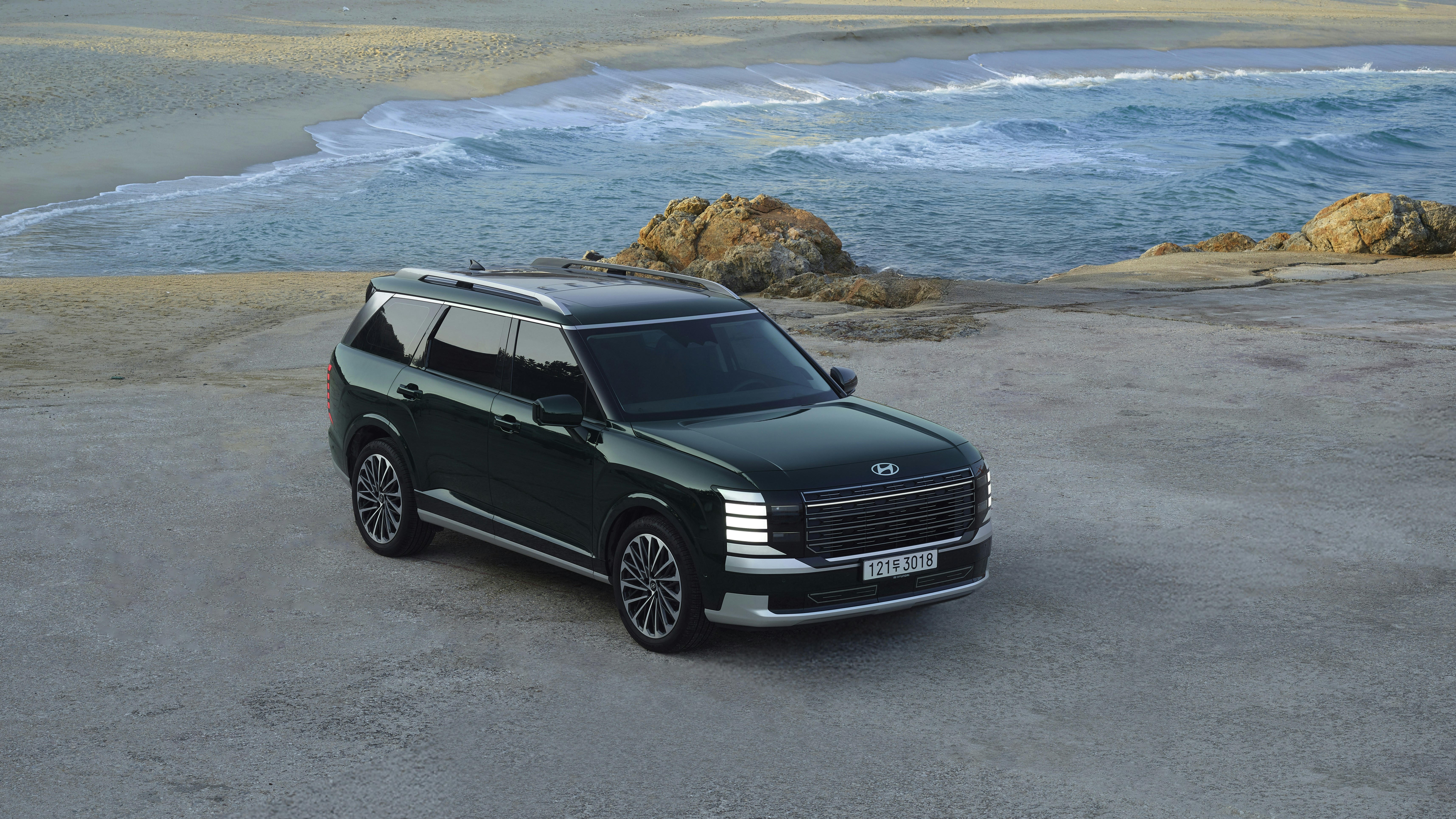 Dark green suv parked on a beach near ocean waves