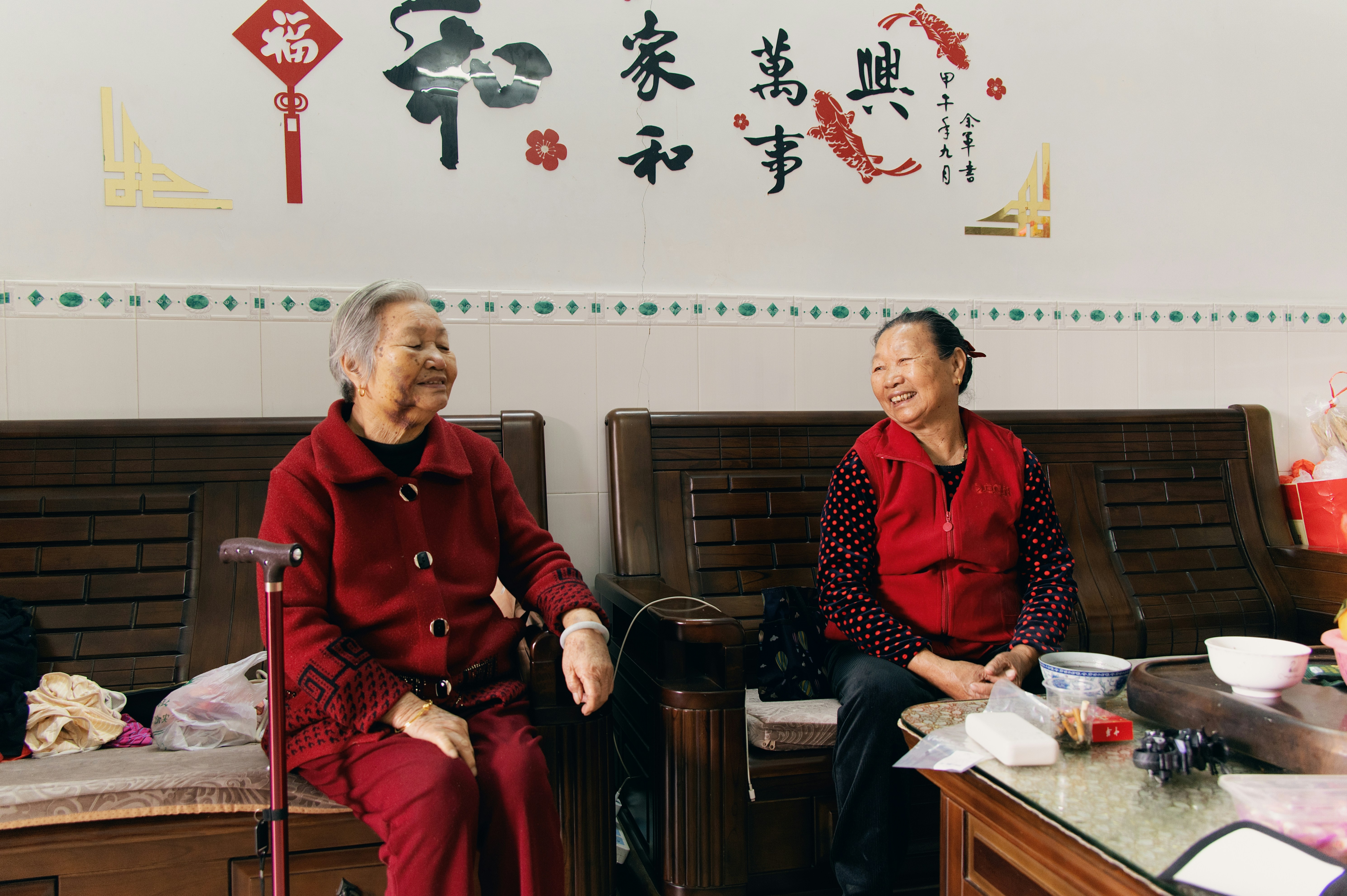 Zwei Frauen in roten Outfits, die auf einem Sofa lächeln.