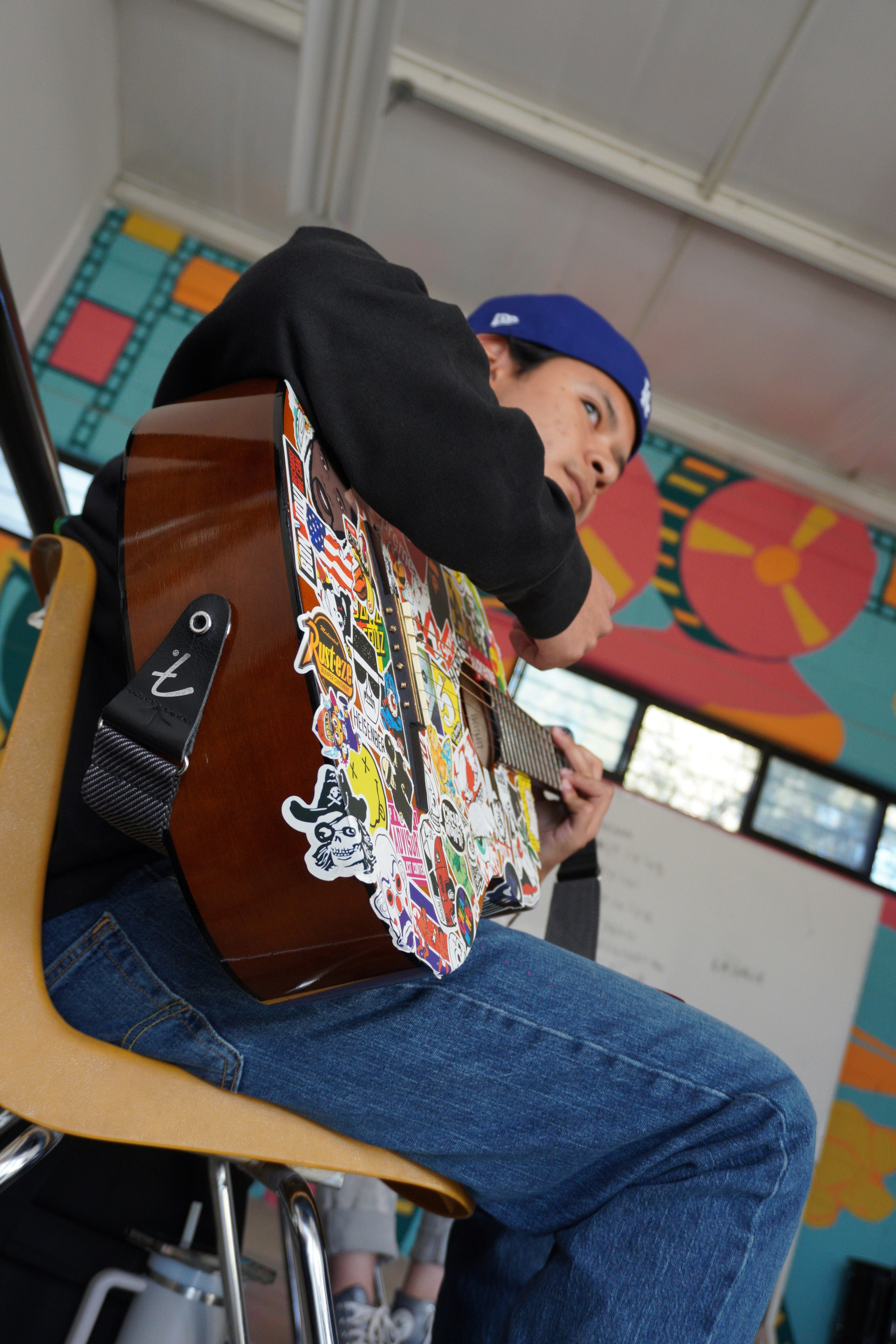 Pria memainkan gitar berlapis stiker sambil duduk.