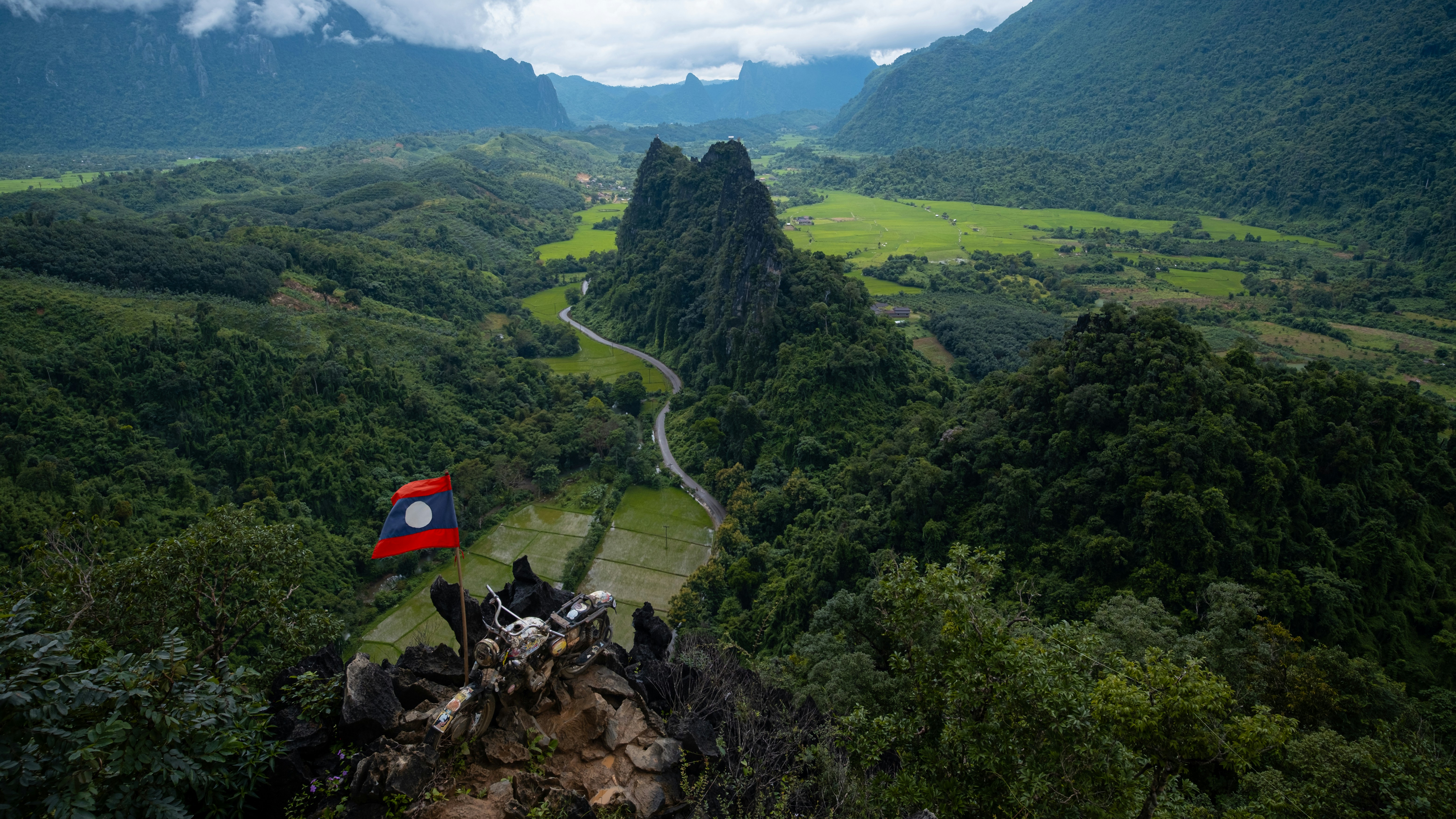Vallée verdoyante avec une route sinueuse et un drapeau