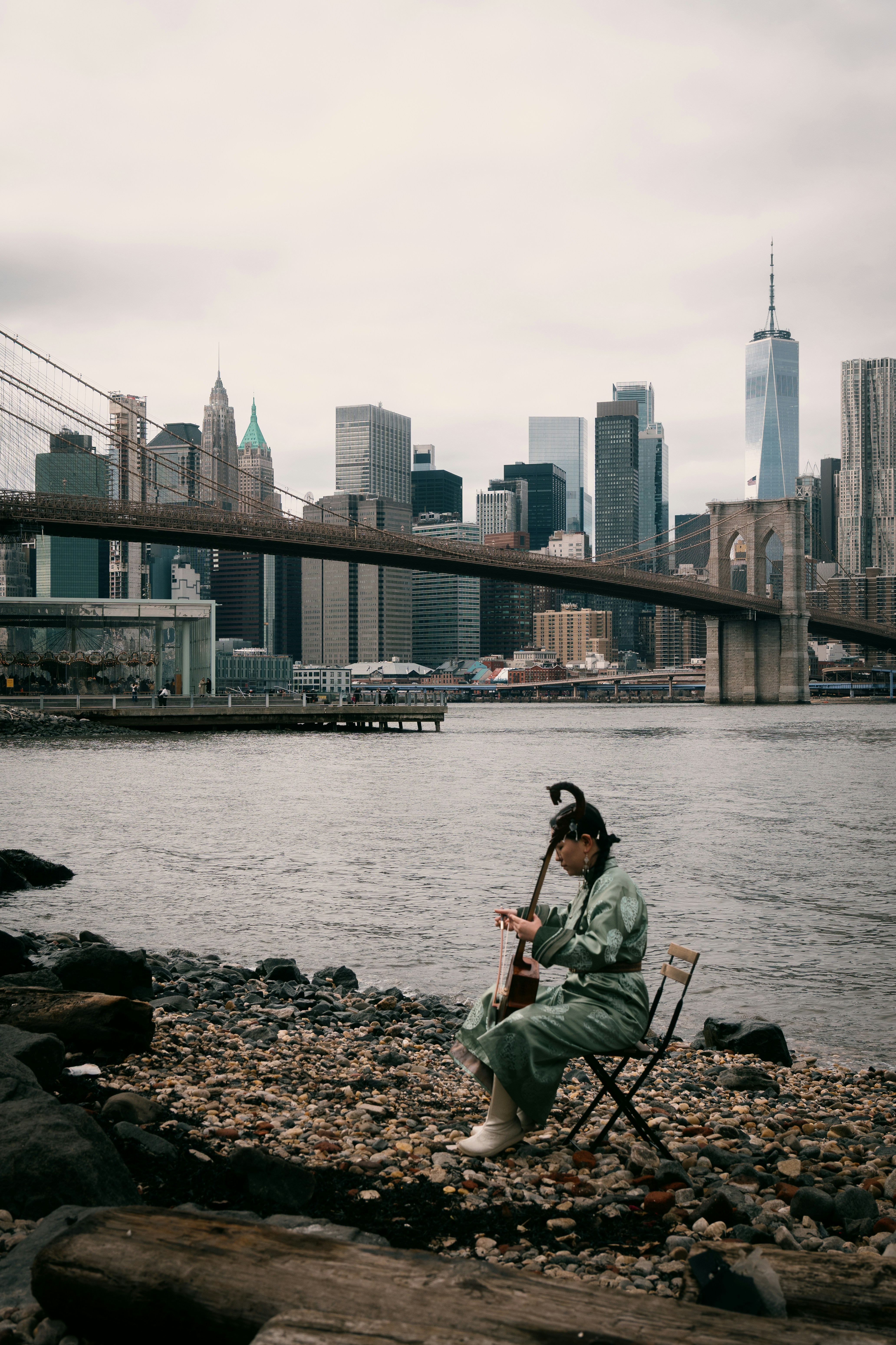 Musician playing instrument by brooklyn bridge with city skyline.