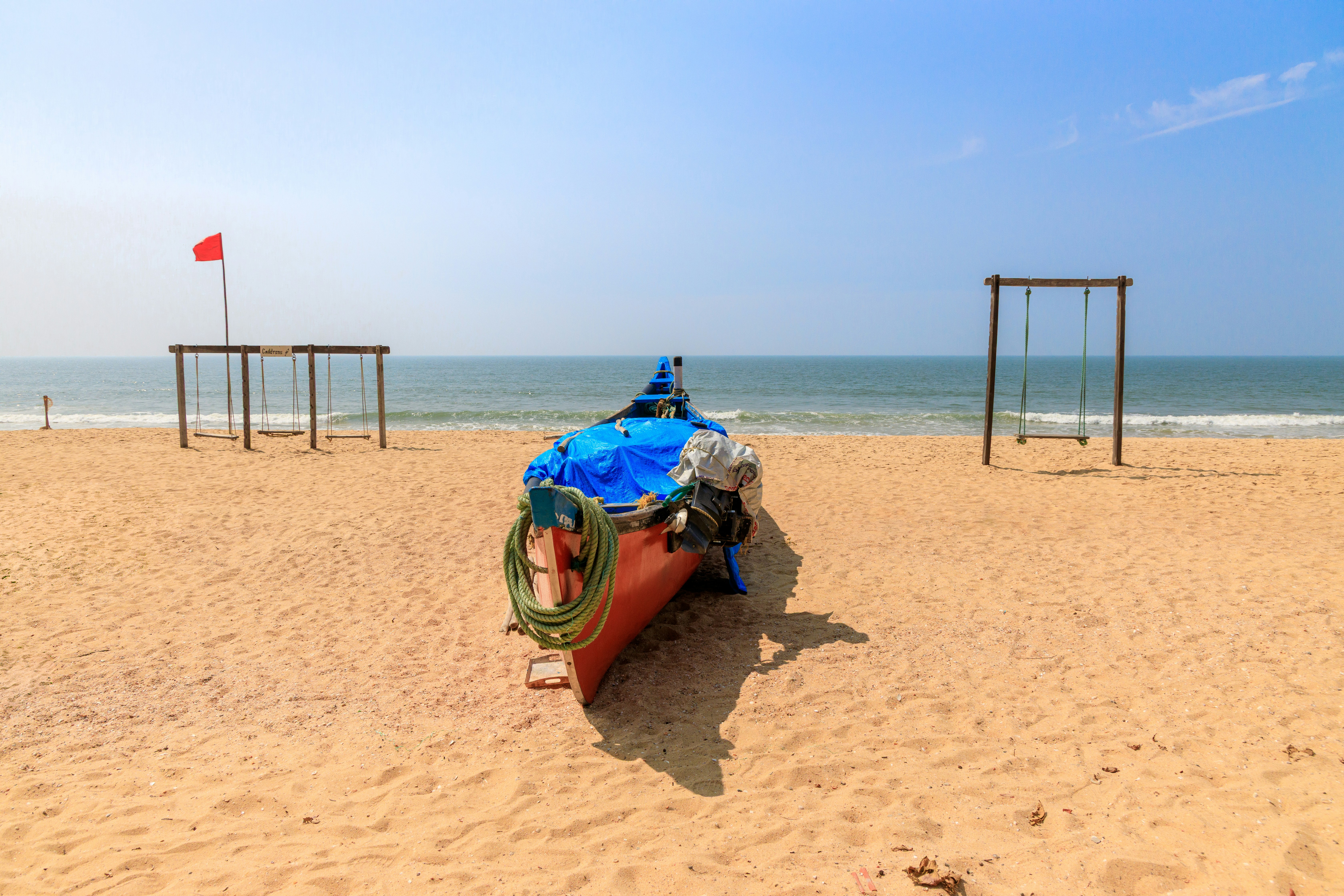 A boat rests on a sandy beach with swings nearby.