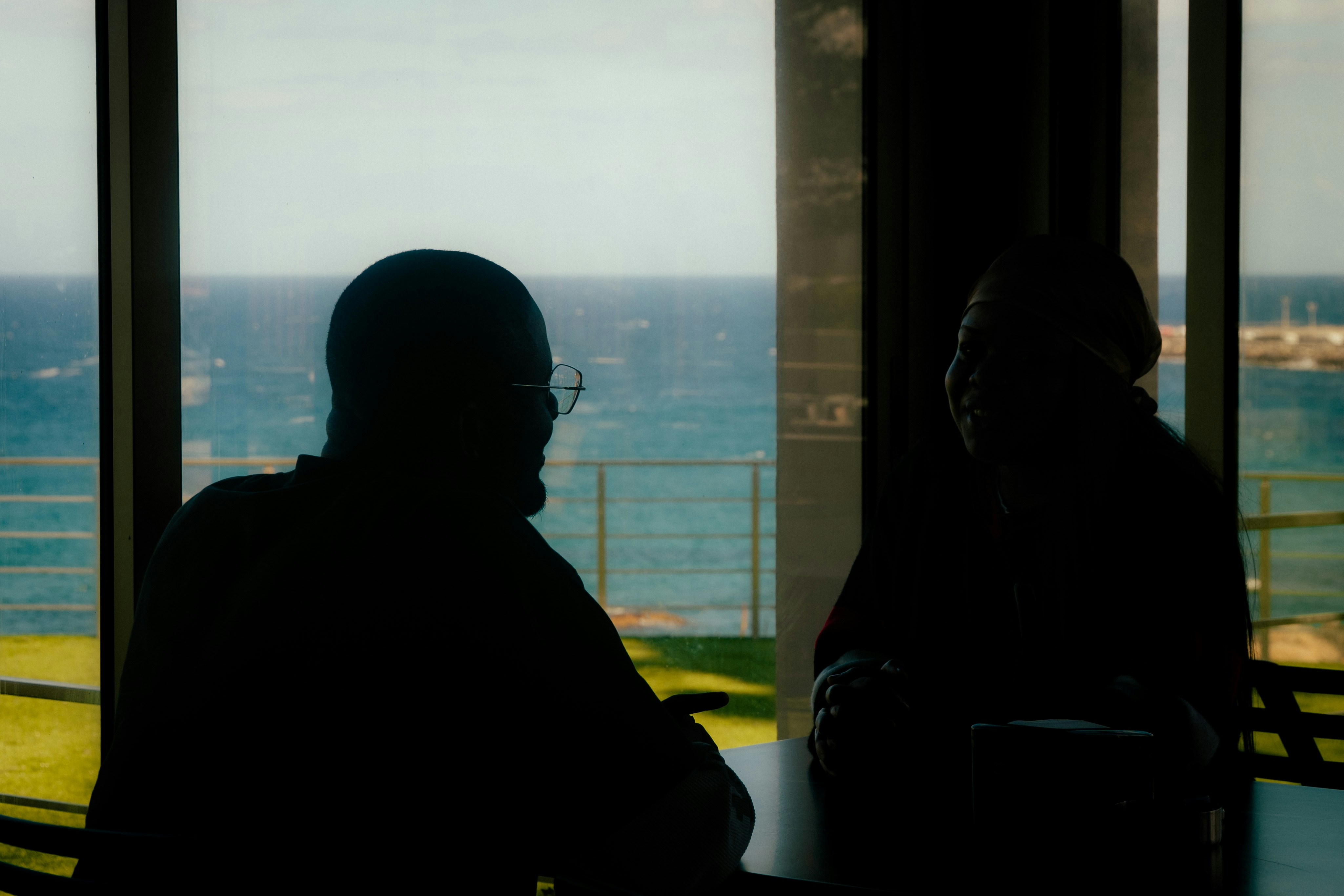 Dua orang dalam siluet di dekat jendela yang menghadap ke lautan.