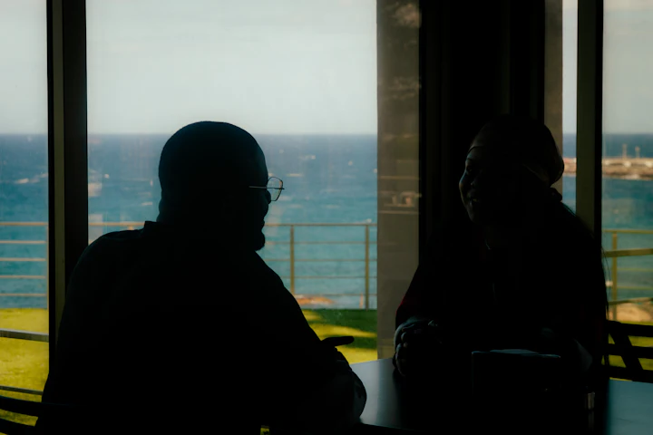 Two people in silhouette by a window overlooking the ocean