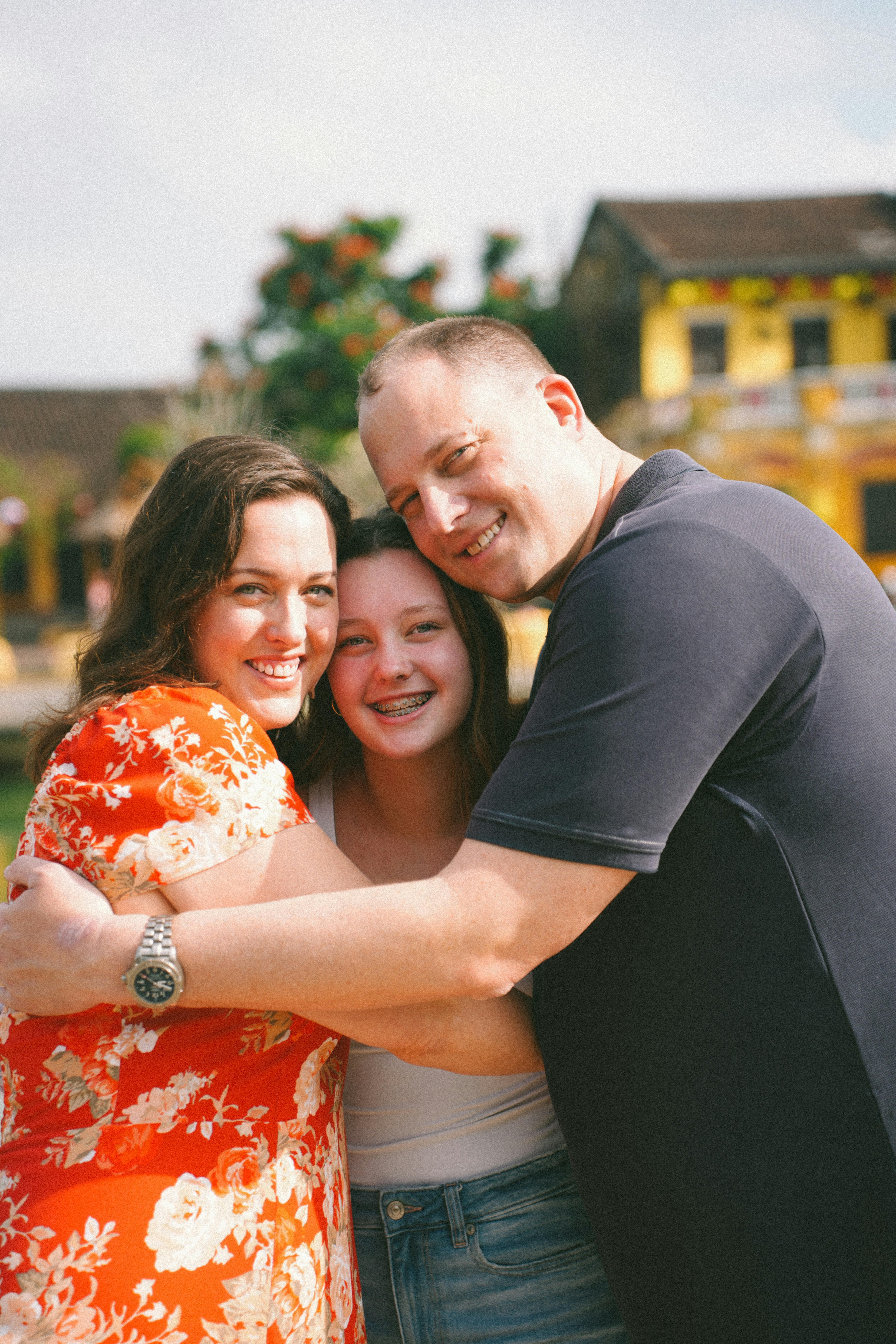 A family of three embracing outdoors on a sunny day.