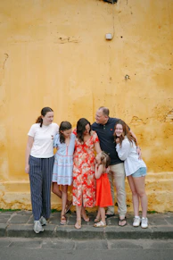 A family of six stands against a yellow wall.