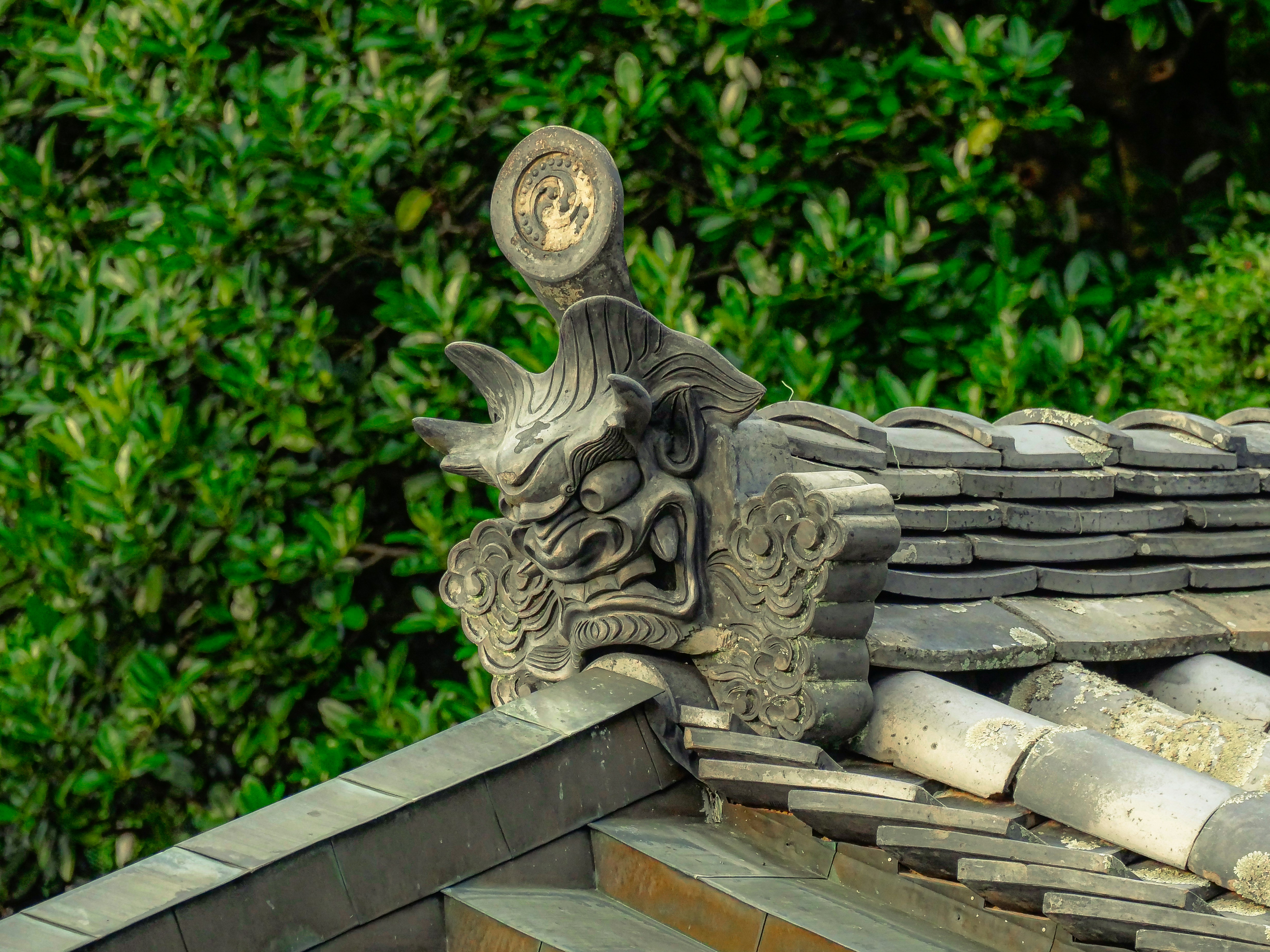 Stone gargoyle on a tiled roof with green foliage.