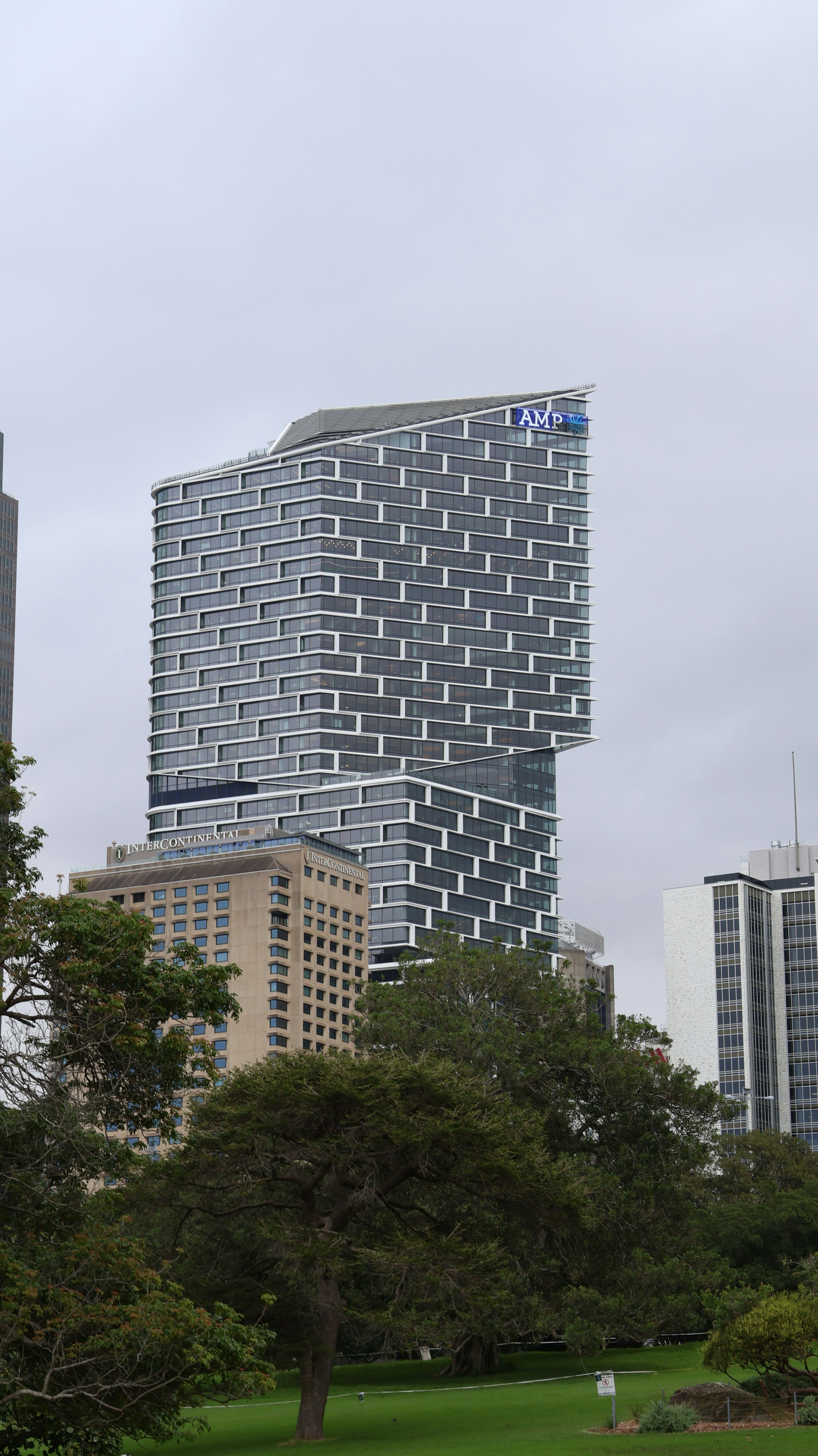 Modern skyscraper with unique facade overlooks park.