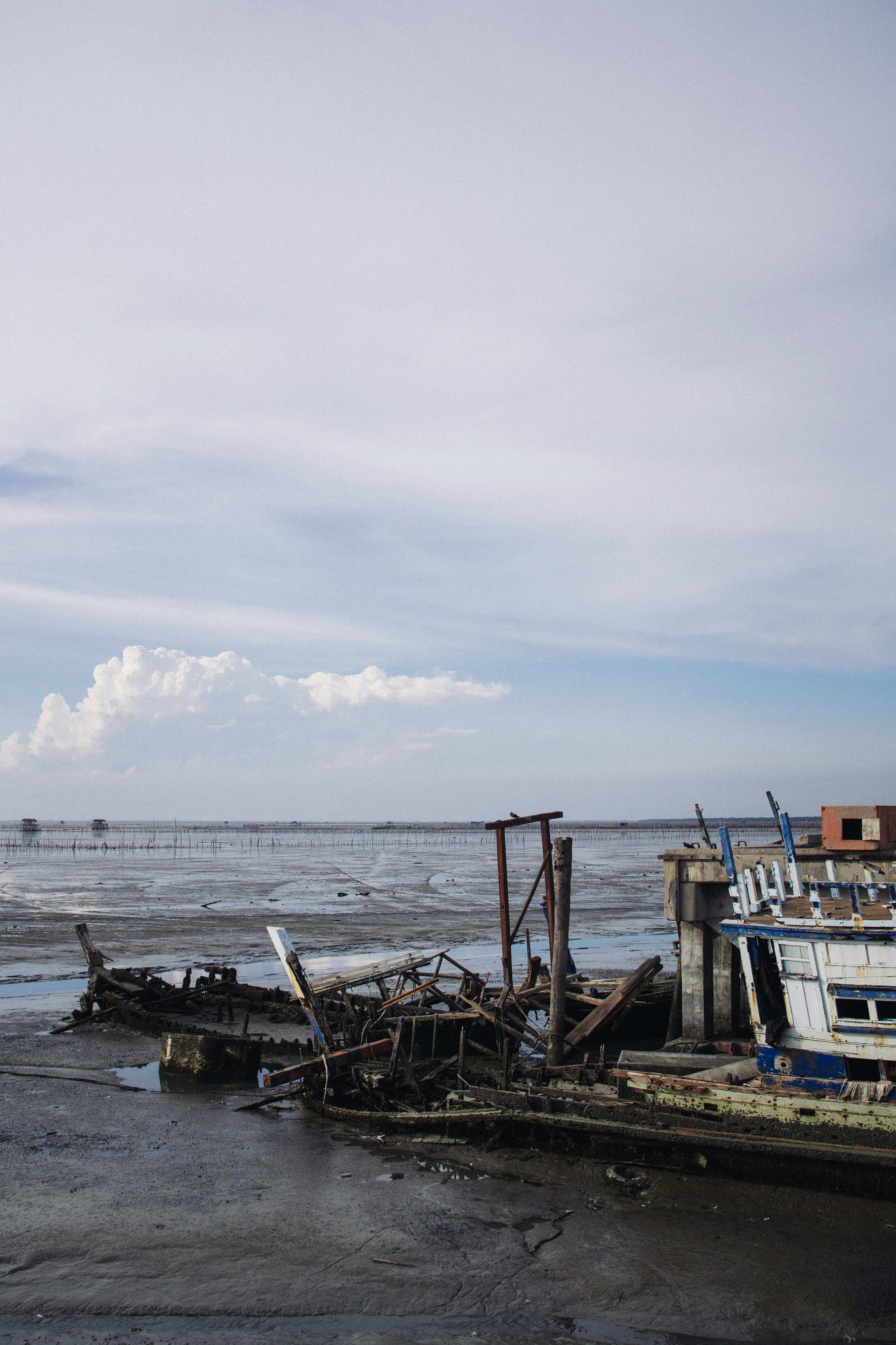 Wrecked boats sit in shallow water under a cloudy sky