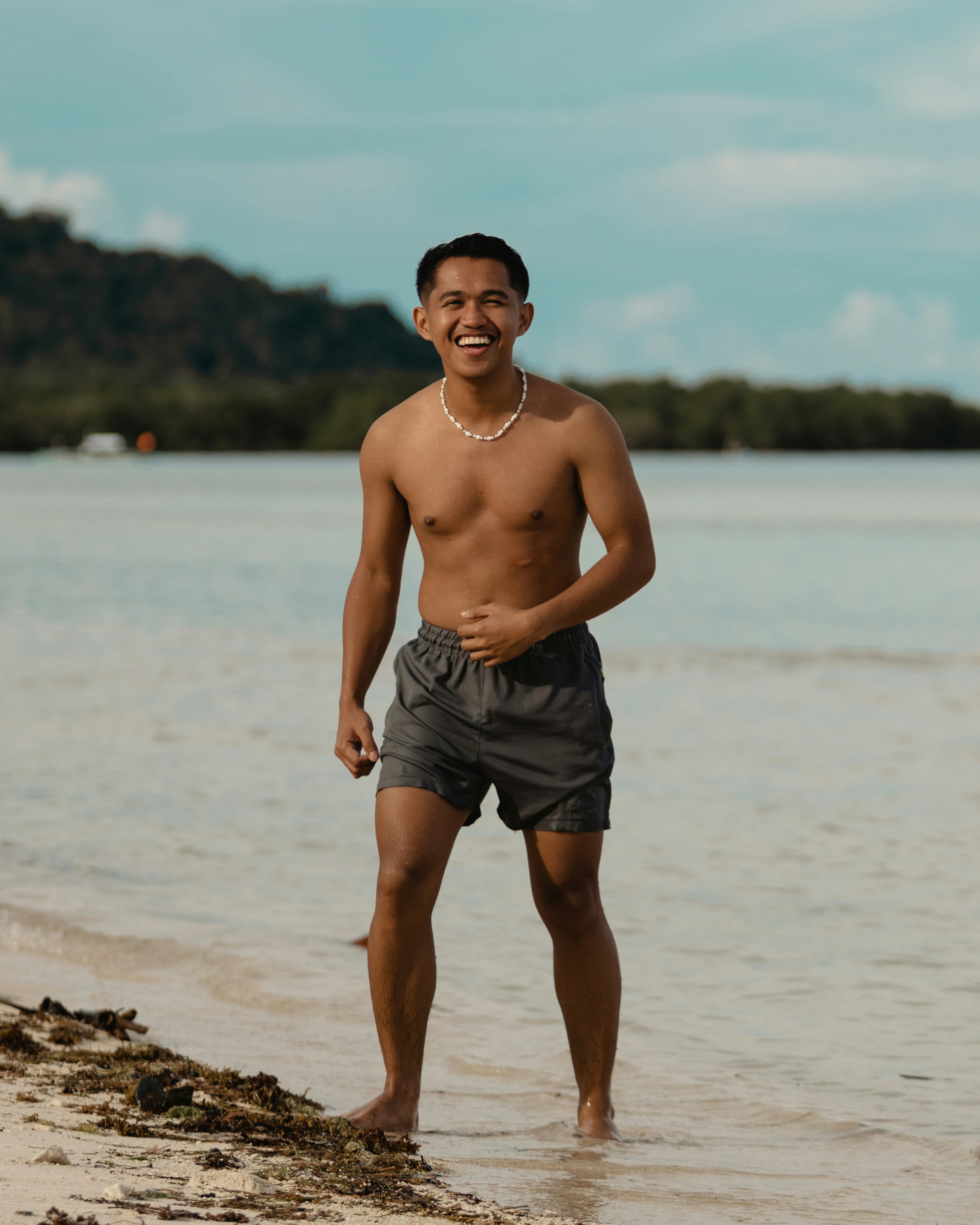 Junger Mann, der am Strand in Shorts lächelt