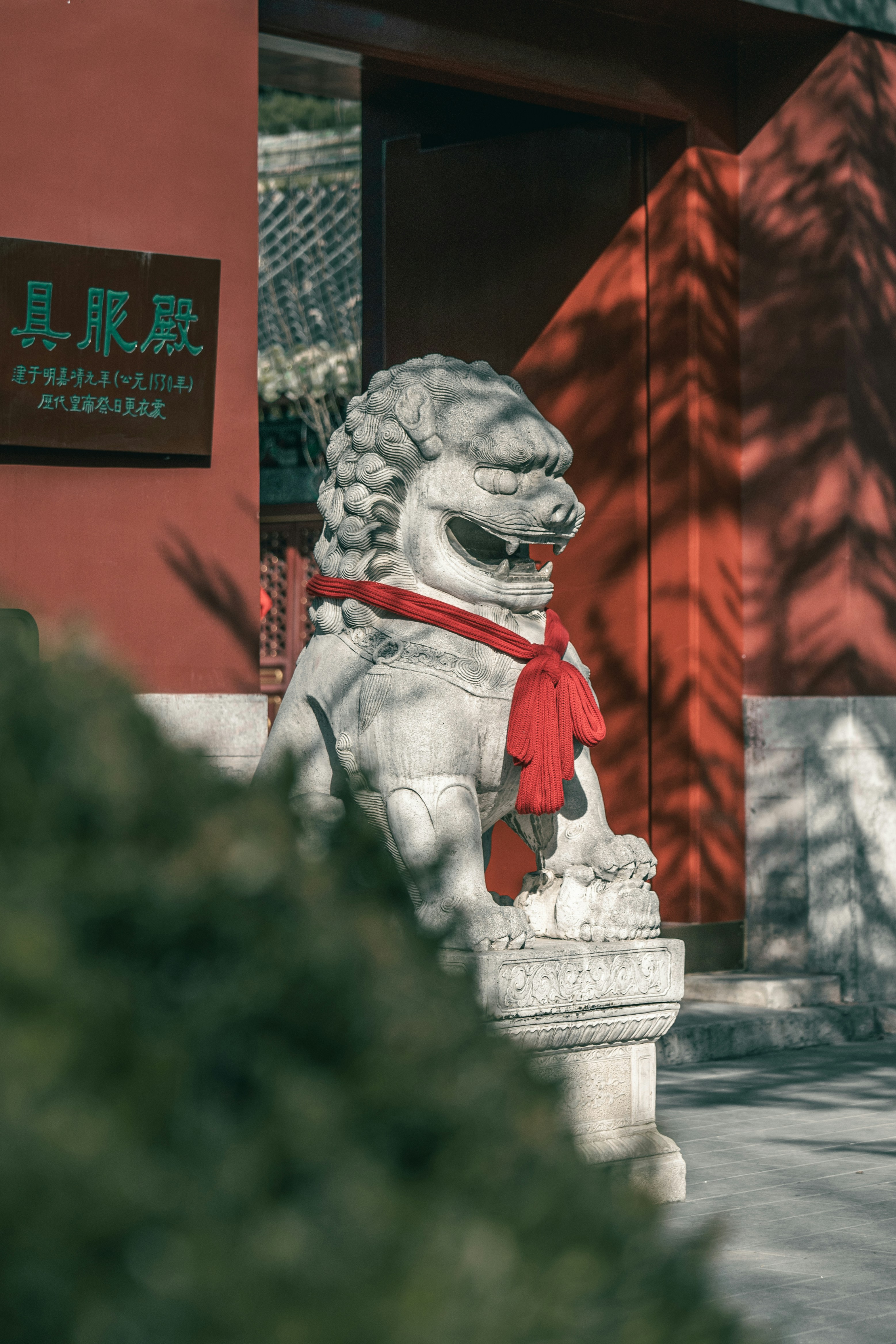 Steinerne Löwenstatue mit rotem Schal vor dem Gebäude