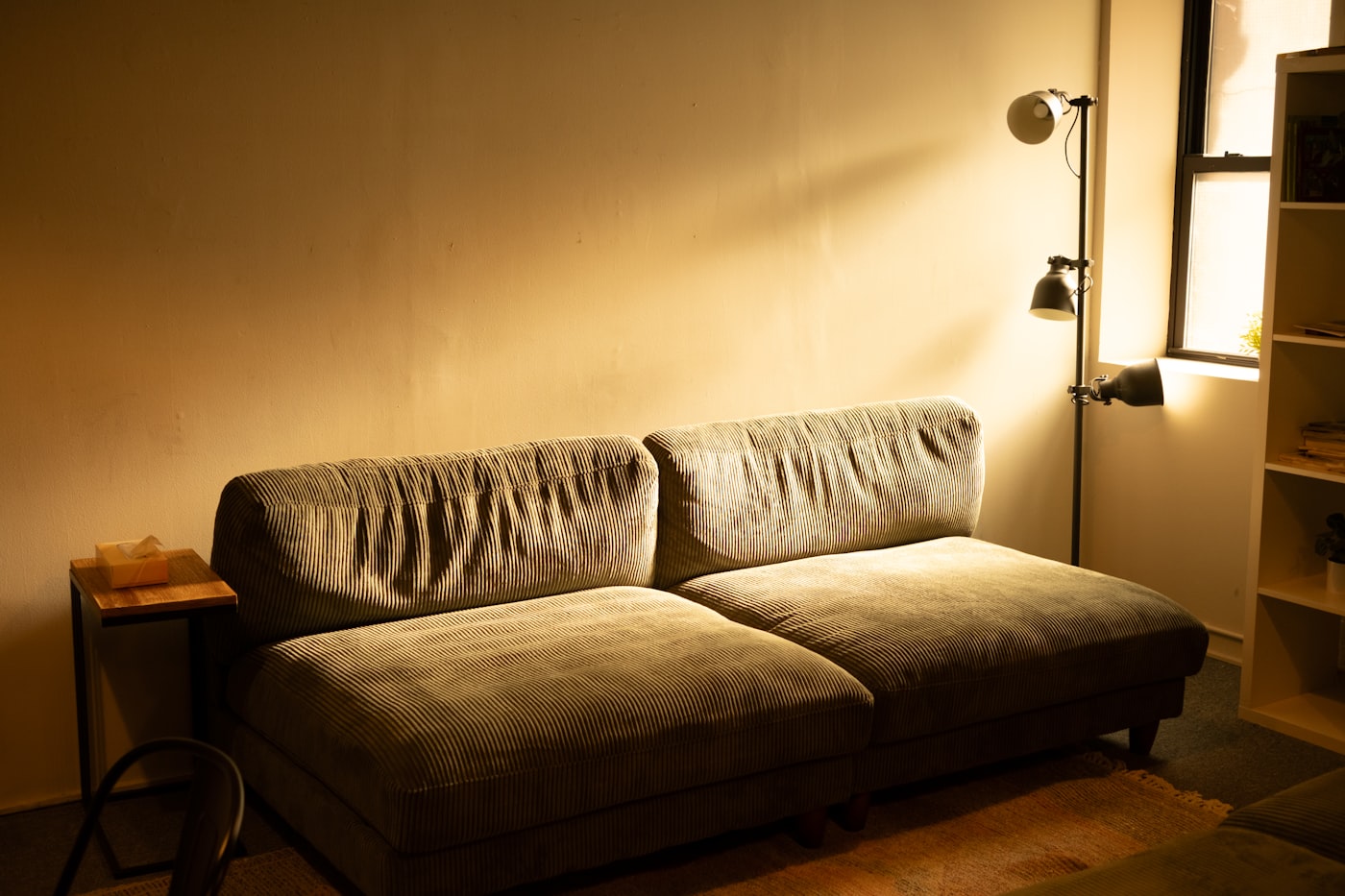 Minimal first apartment living space with a small corduroy sofa and warm floor lamp for a college grad