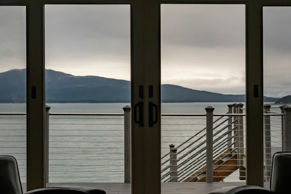 View of a calm sea and mountains through glass doors.